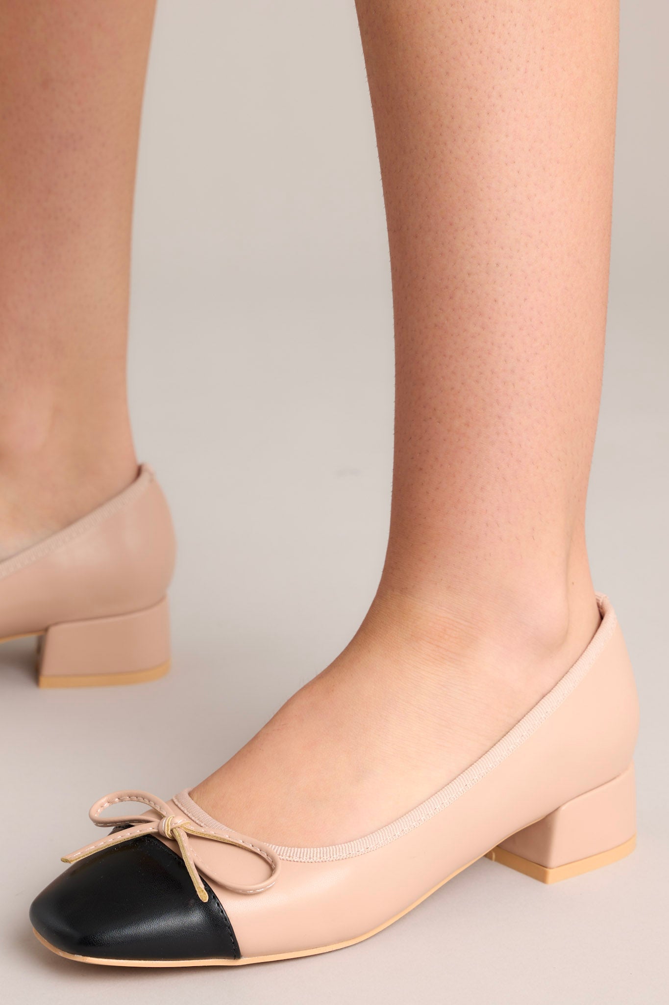 Full side profile of beige heels on a grey background, emphasizing the elegant curve and two-tone design.