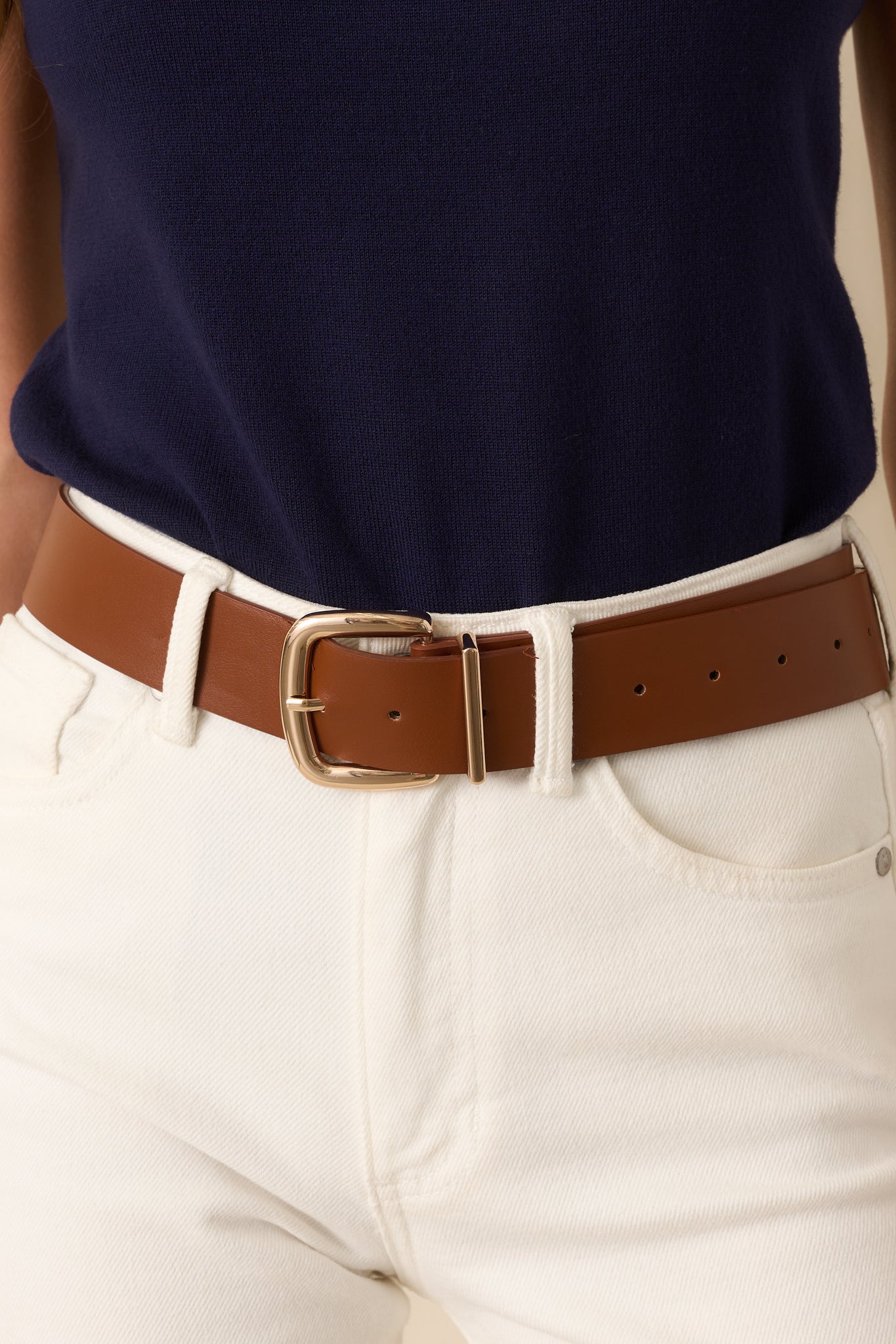 Cropped view of the cognac brown belt showing the gold-tone square buckle and stitched faux leather material.