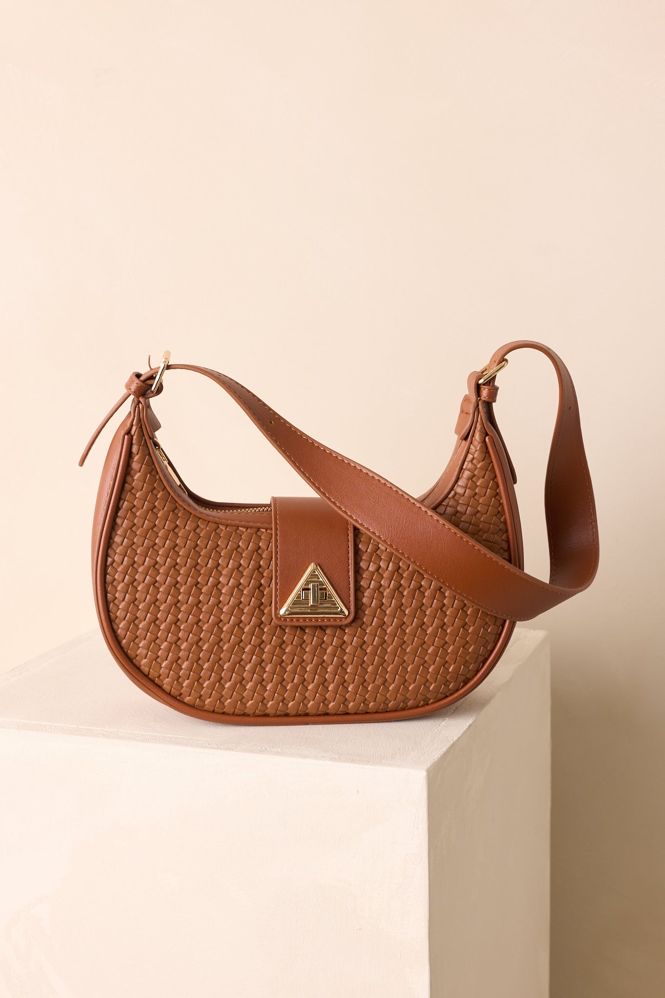 Close view of woven faux leather material and gold triangular twist-lock closure on curved flap.