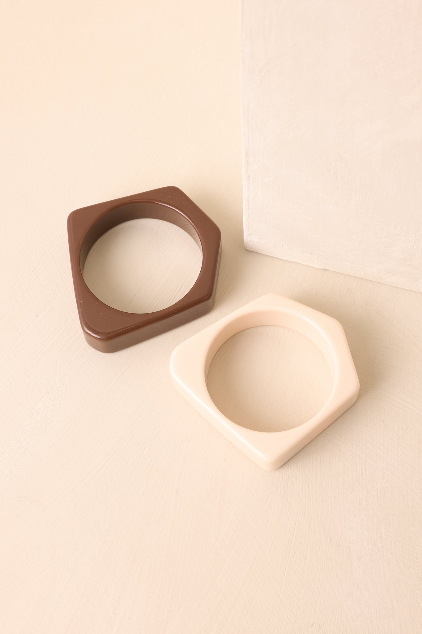 A shot of the cream and brown wide bangles with square edges displayed together against a beige background.