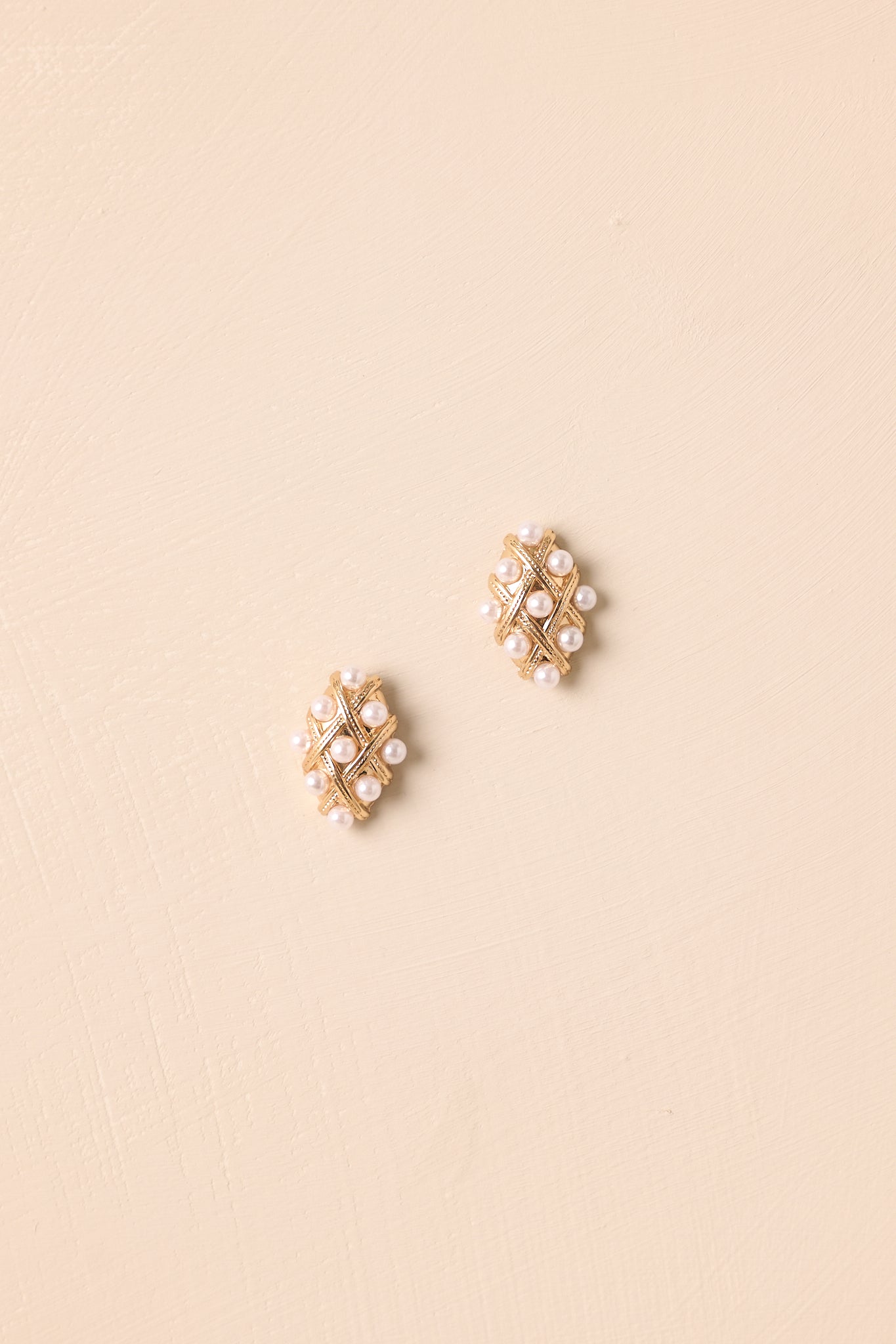 Overhead view of these gold & faux pearl earrings that feature a diamond shape, gold hardware, a quilted design, faux pearls accents and secure back postings.