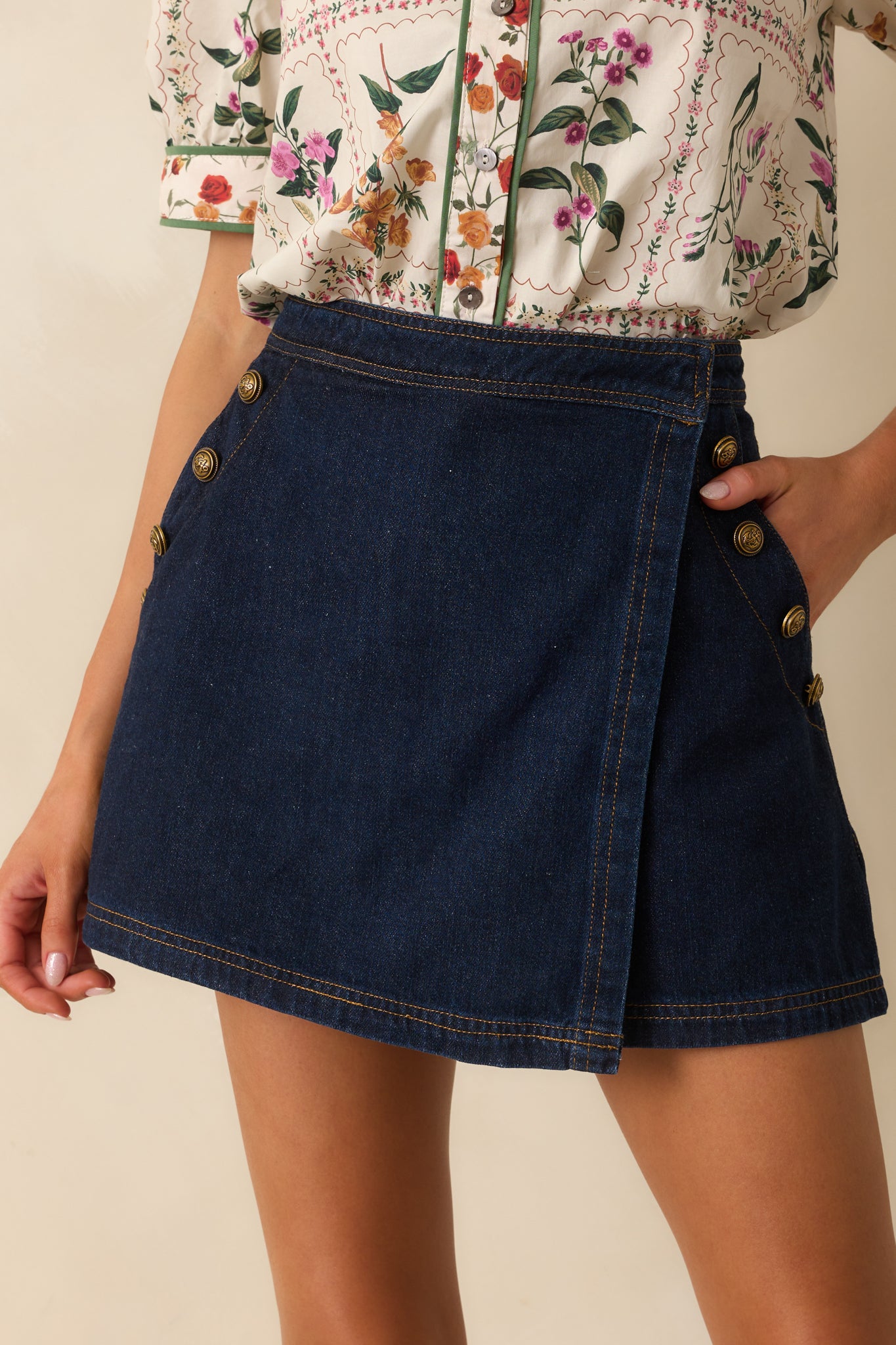 Close-up showing the dark wash skort’s hook-and-bar closure, tan topstitch detailing, and embossed gold buttons on side pockets.