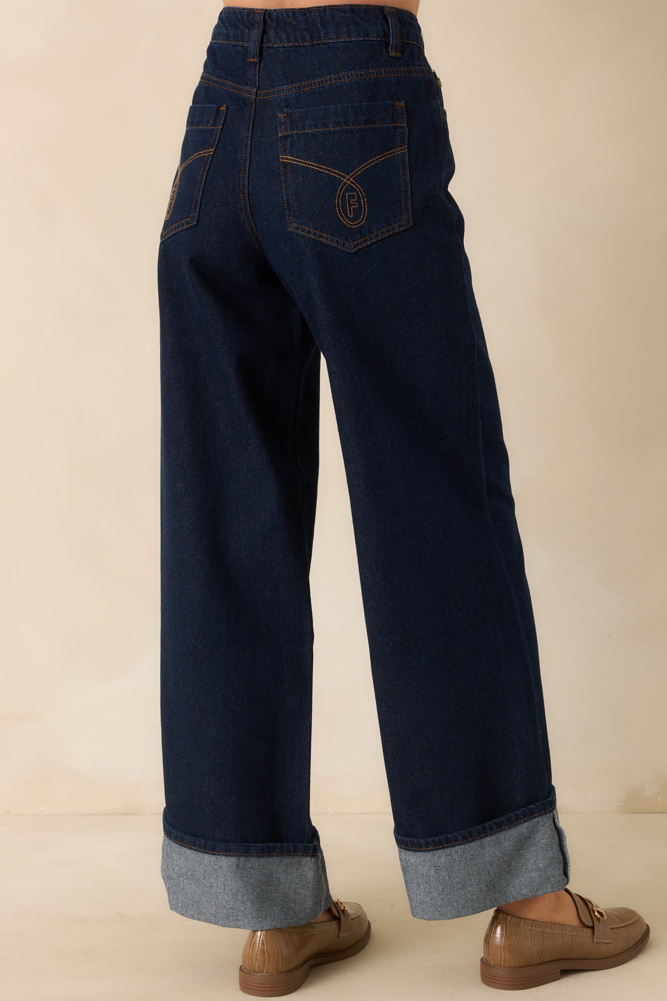 Rear view of dark wash jeans highlighting back pockets, belt loops, and sewn hem cuffs from the back.