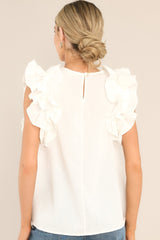 Back view of this ivory top that features a high crew neckline, a keyhole with a button closure at the back of the neck, and ruffled shoulder detailing.