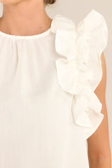 Close up view of this ivory top that features a high crew neckline, a keyhole with a button closure at the back of the neck, and ruffled shoulder detailing.