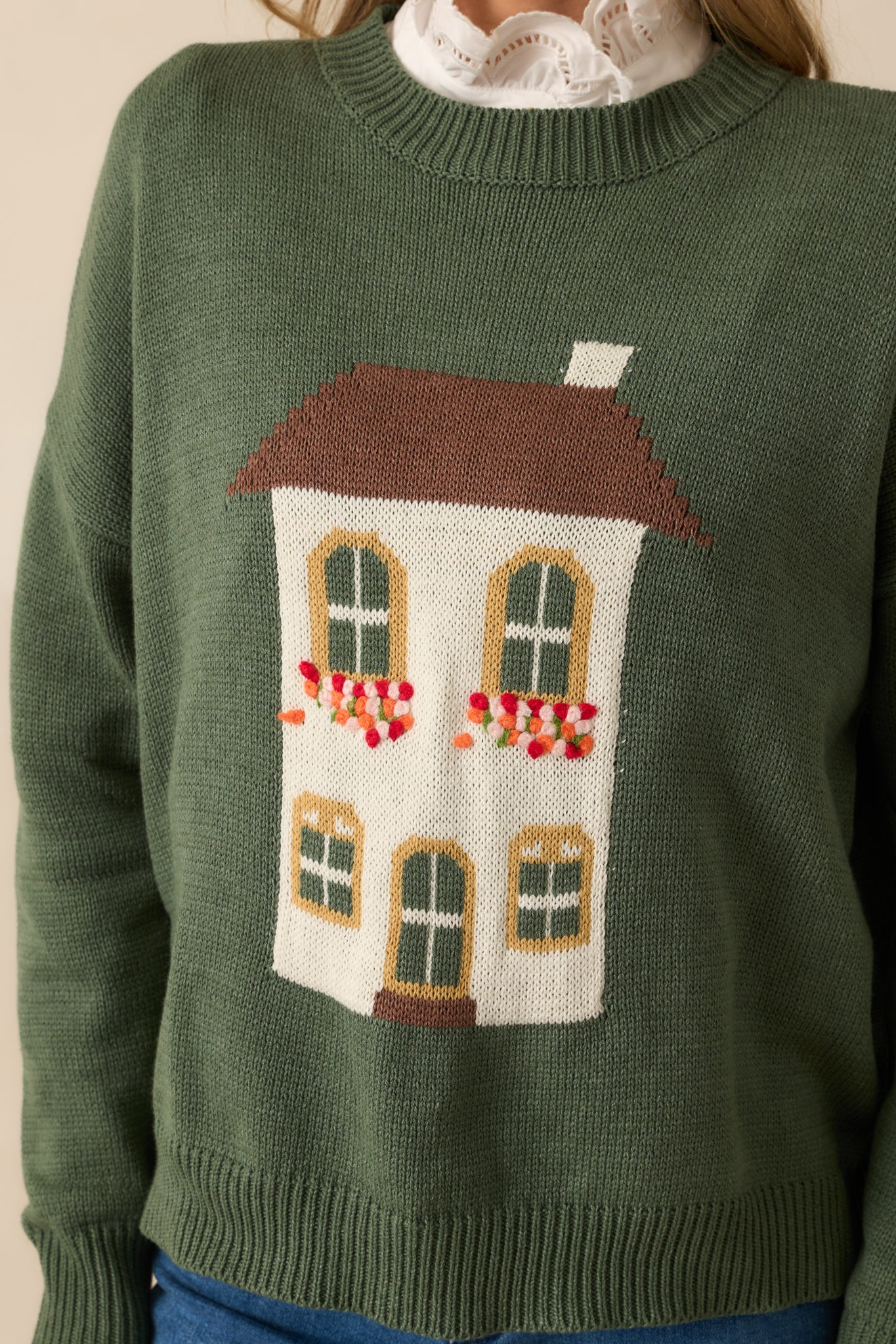 Detailed close-up of green sweater’s cotton-blend knit fabric with textured house motif design.