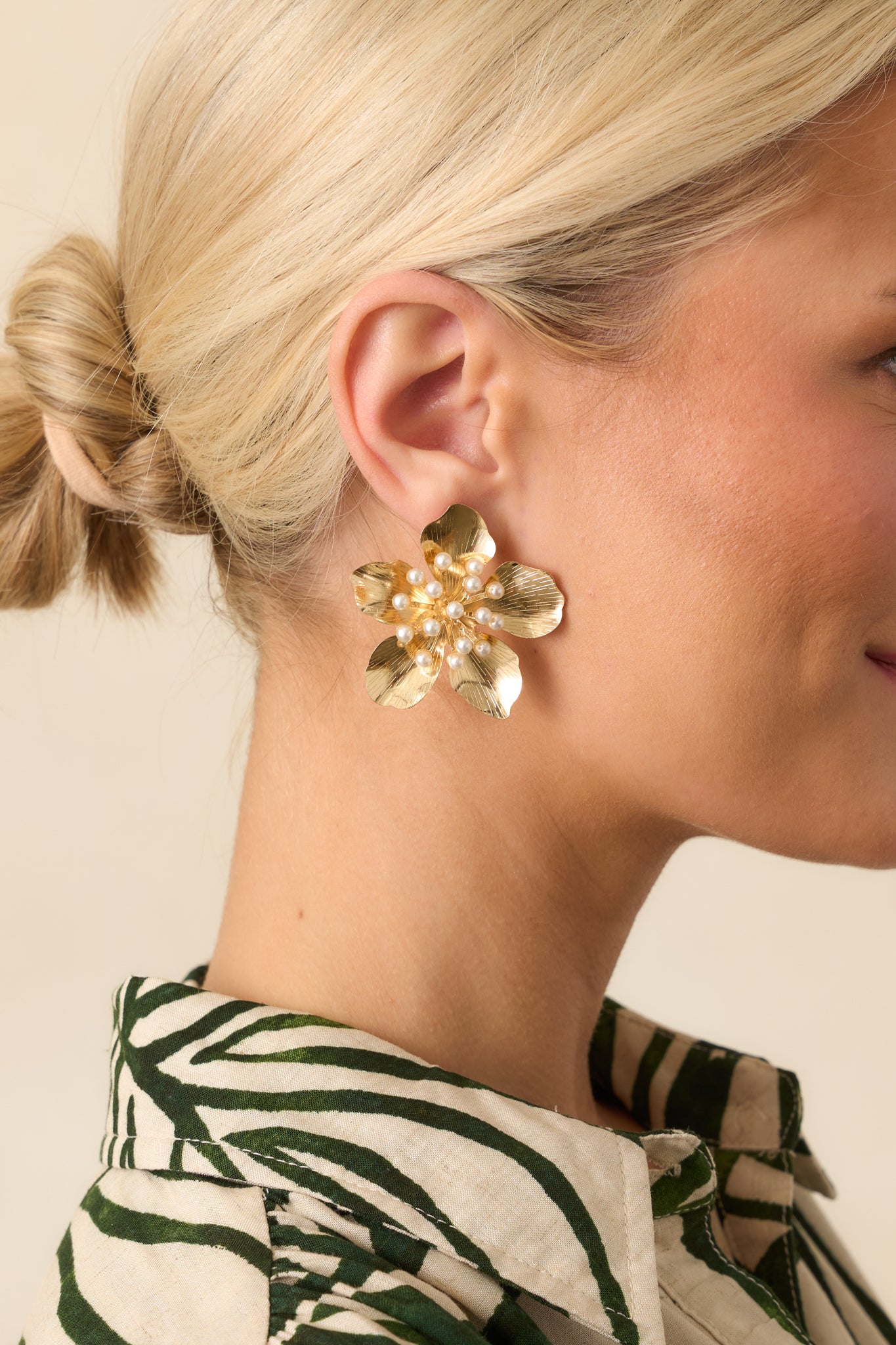 A close-up crop of the earrings worn, showing the five textured gold petals and the clustered ivory faux pearl center.