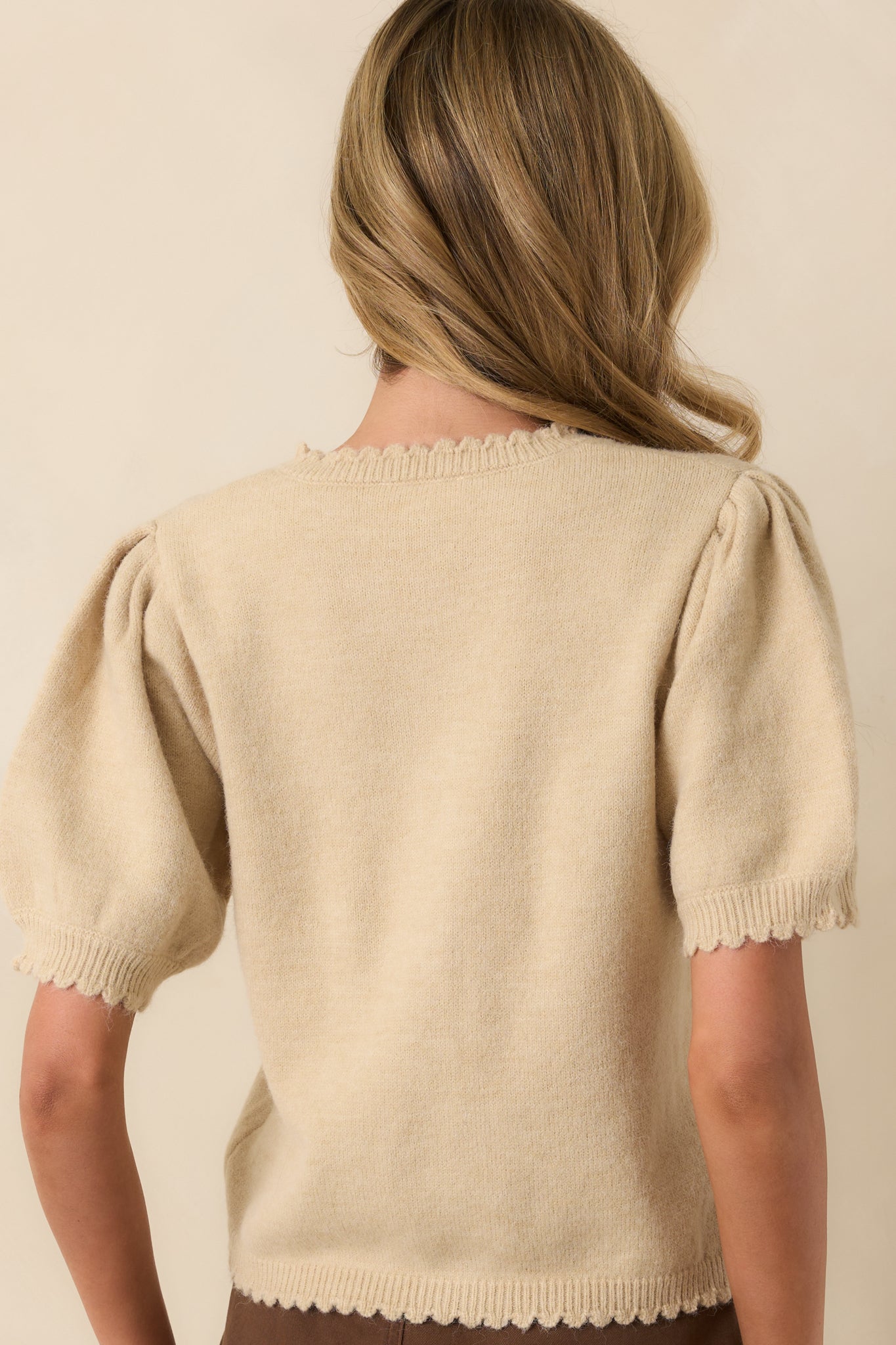 A view from behind showing the smooth knit fabric, short sleeves, and ribbed hemline of the ecru Beige cardigan.