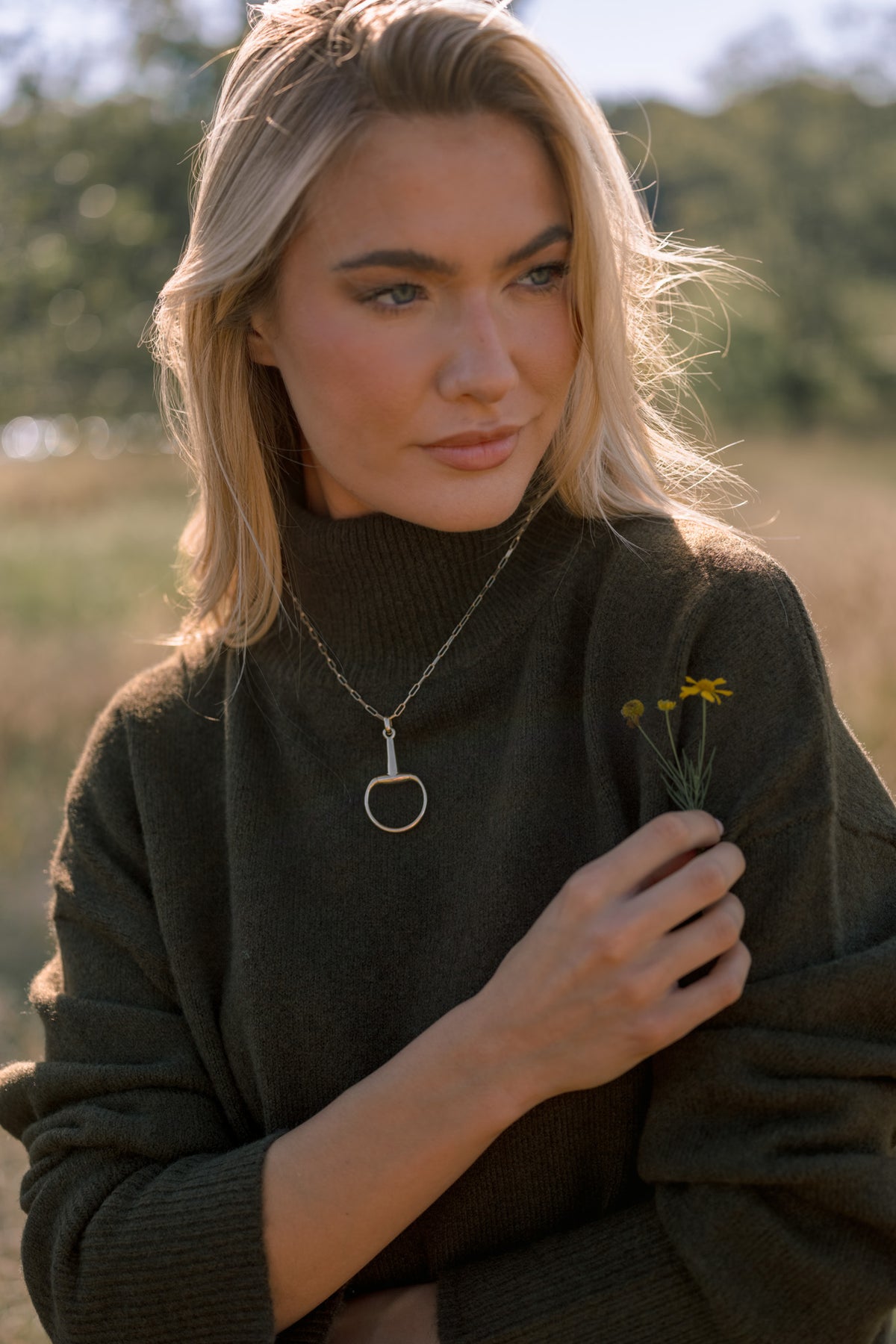 Rein It In gold horsebit pendant necklace with an elongated-link chain and open circular pendant, shown on a model.