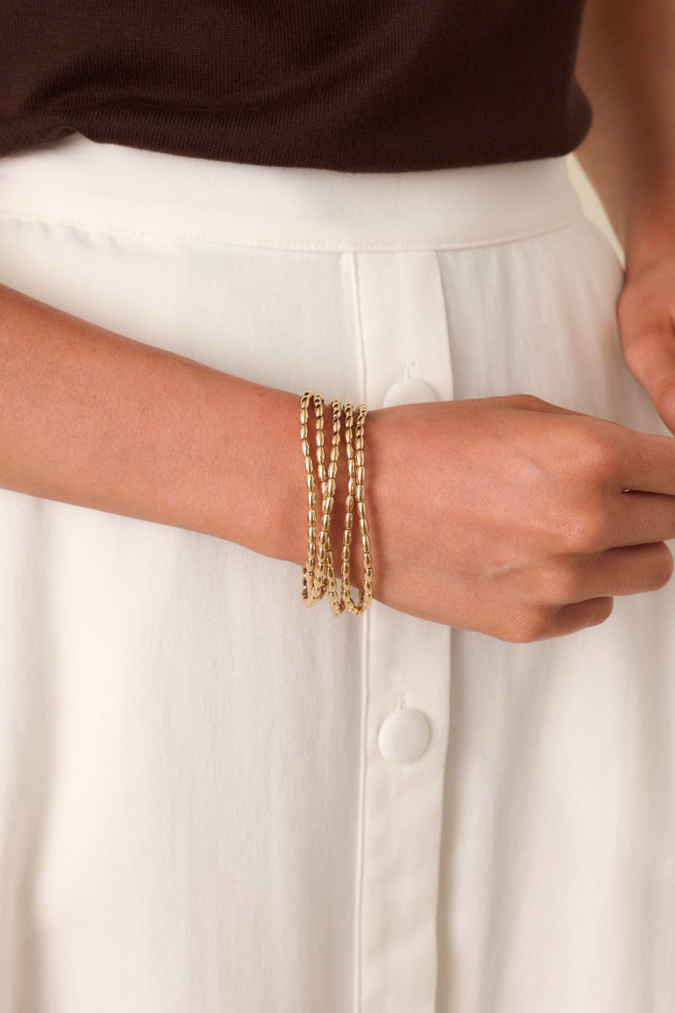 Cropped view of the gold beaded bracelet set showing multiple stretchy bands with elongated oval beads and a polished finish.