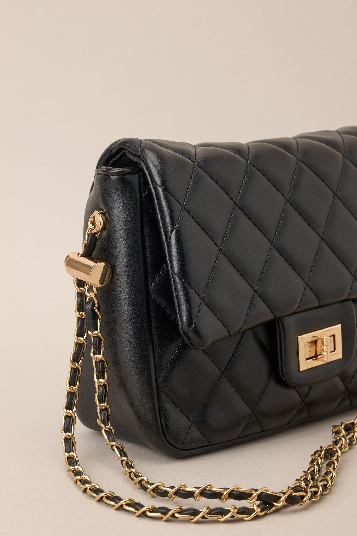 Close-up view of this black bag that features gold hardware, a quilted texture, a twist lock closure, a zipper pocket inside, and an adjustable chain strap.