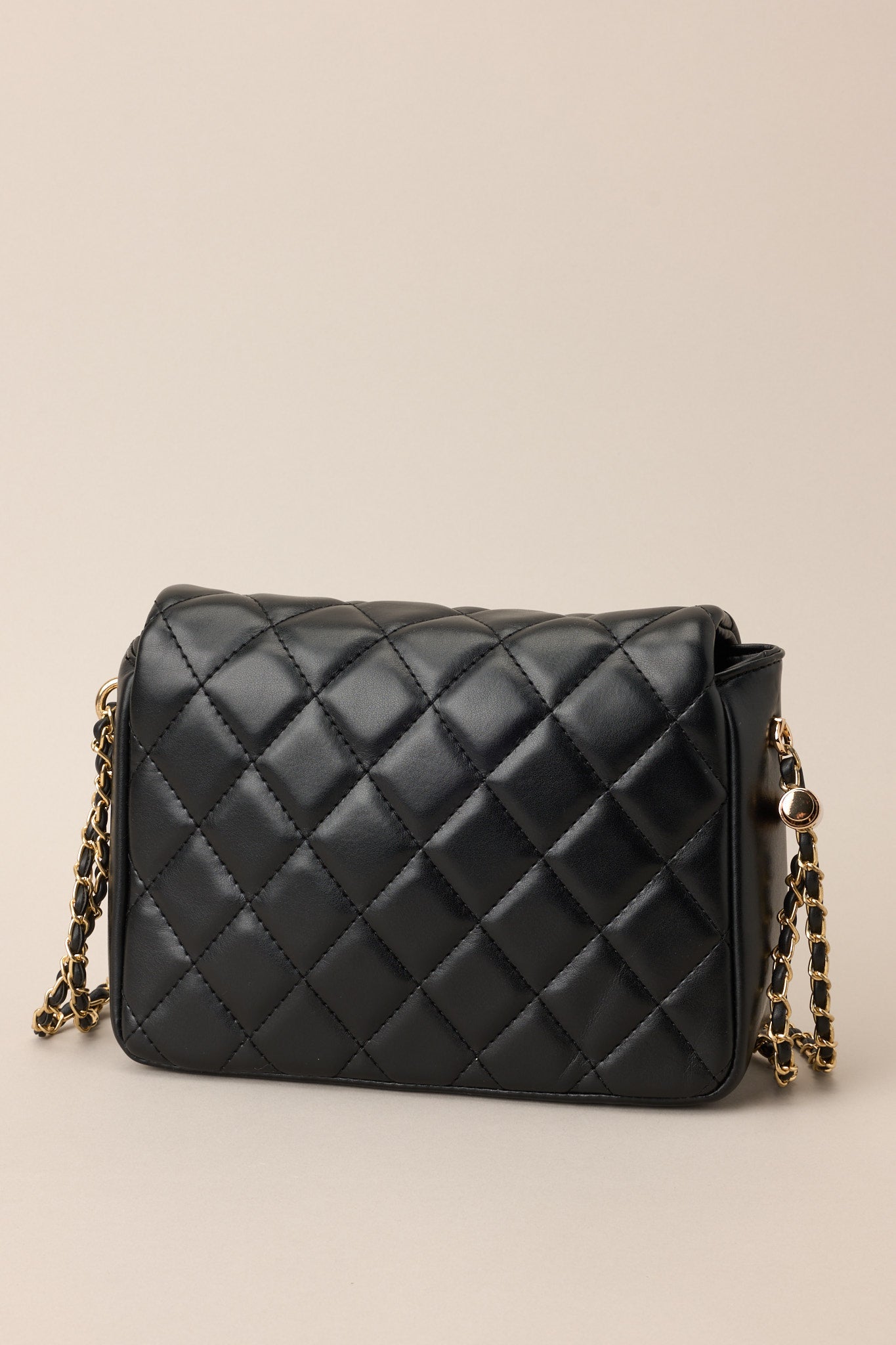 Back view of this black bag that features gold hardware, a quilted texture, a twist lock closure, a zipper pocket inside, and an adjustable chain strap.