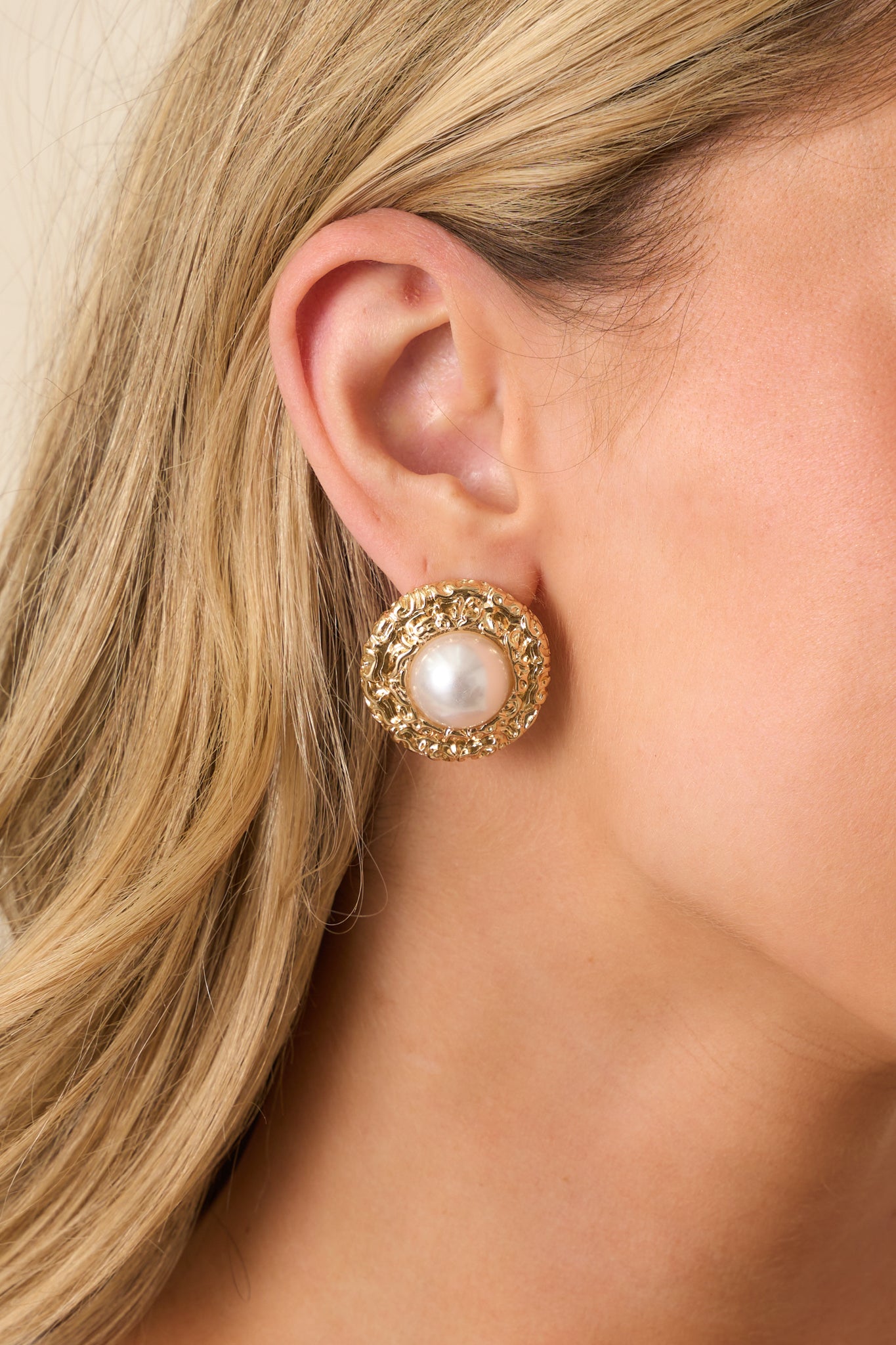 A close-up detail shot of the earrings showing the domed faux pearl and intricate textured gold border.