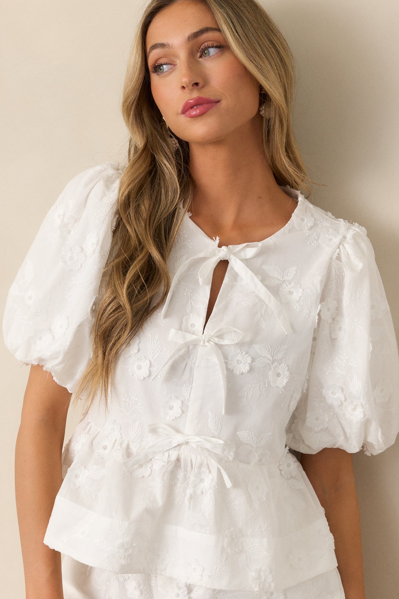 A focused view of the blouse’s bow front detail, puff sleeves, and peplum bottom, showcasing the soft white fabric and feminine cut.