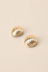 Angled overhead view of these gold earrings with circular shape, wave-like texture, secure post backing.