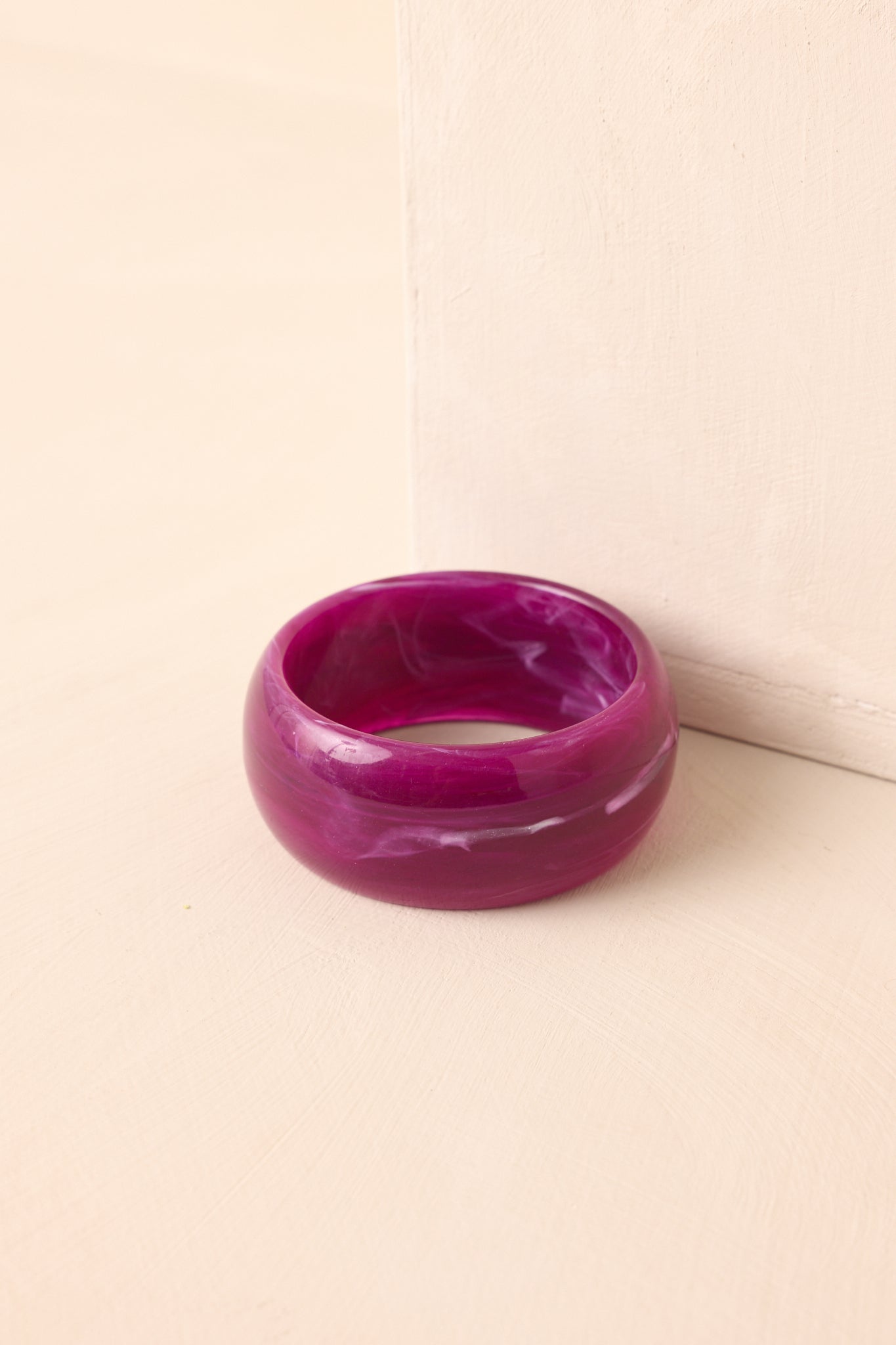 Glossy wide purple bracelet with a bold marbled look resting against beige background.
