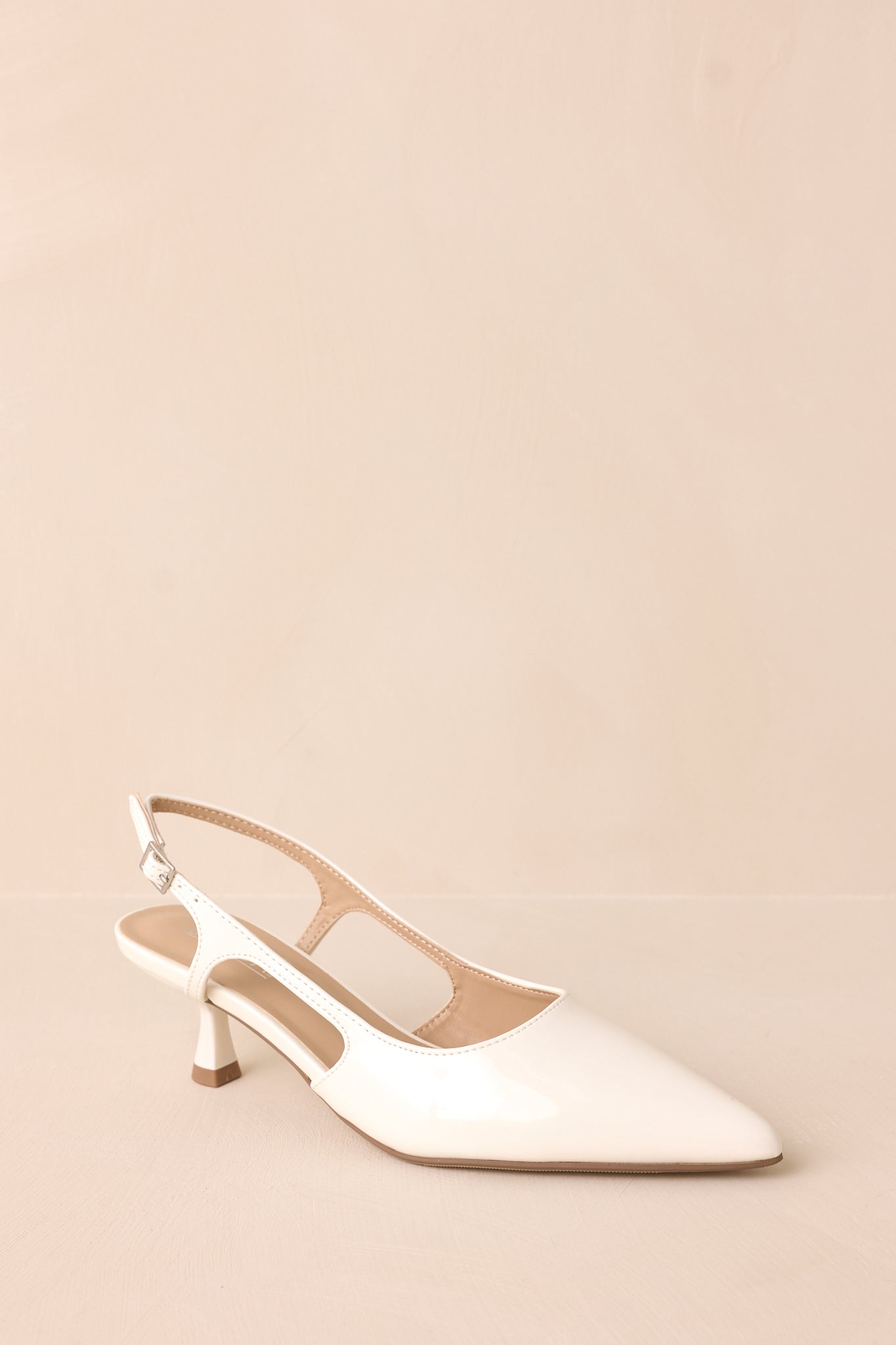 Gold buckle white patent pointed-toe heel with side cutout angled side view on backdrop.