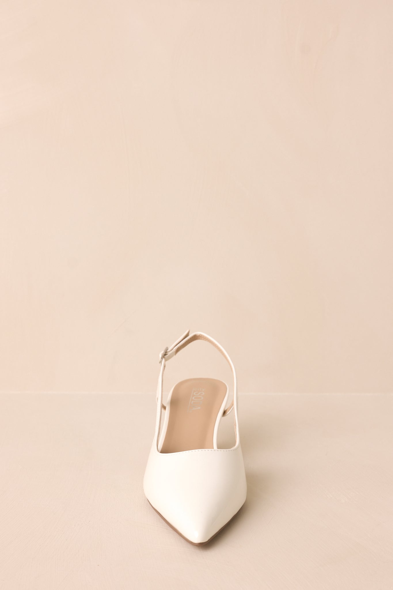 Gold buckle white patent pointed-toe heel with side cutout front view.