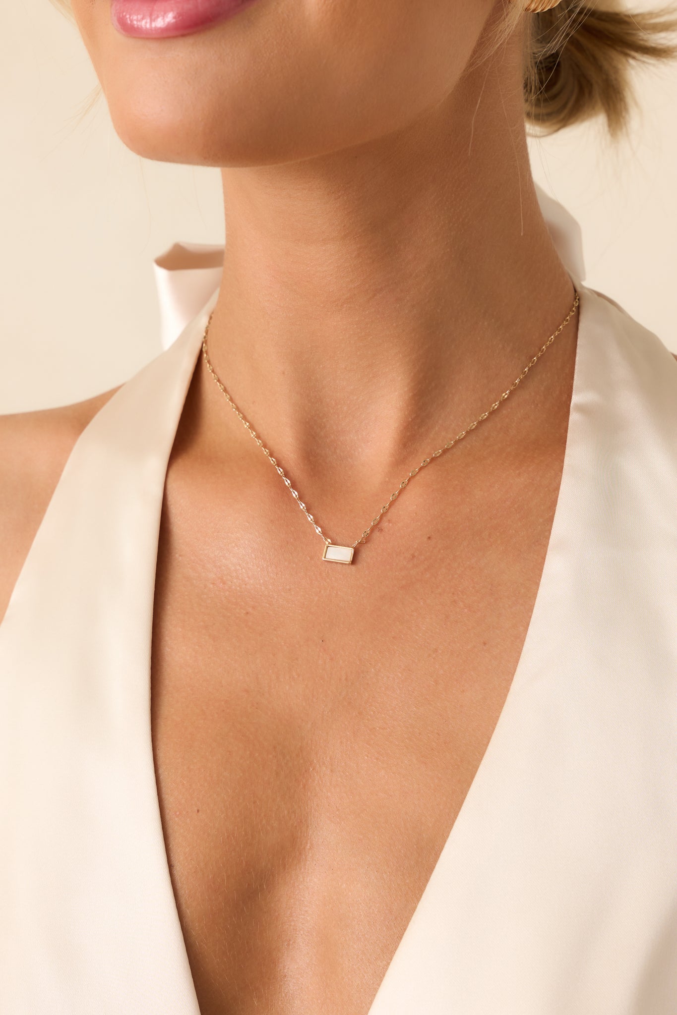 A cropped image showing the thin gold chain and the ivory pearlescent rectangular pendant resting at the center.