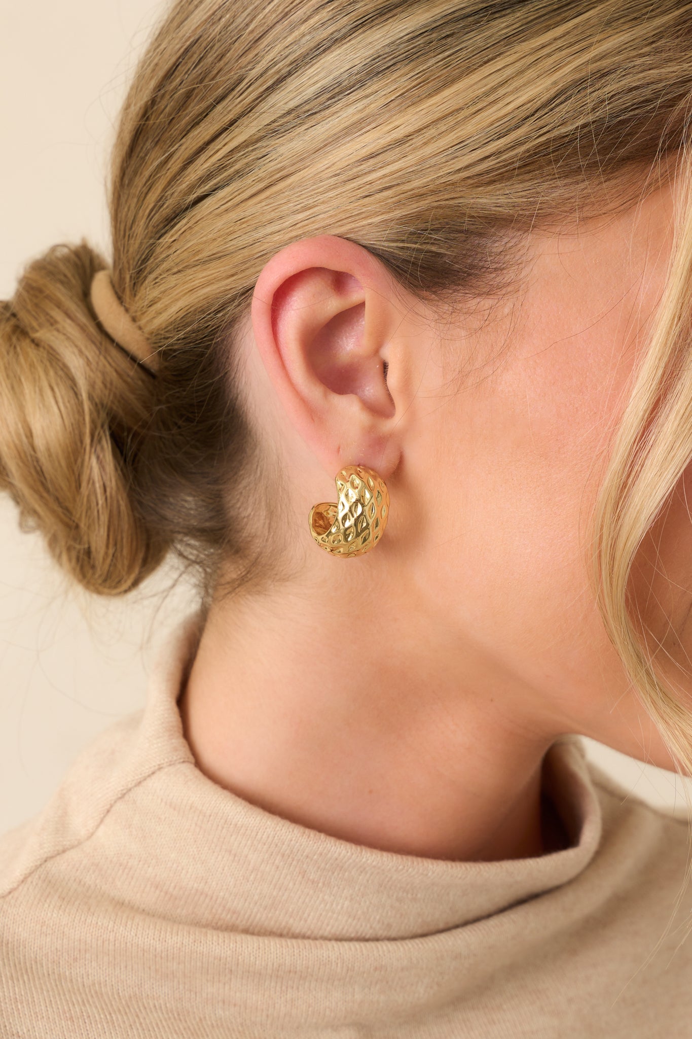Close-up of a pair of gold earrings featuring a chunky small open hoop design with subtle dimpled indents throughout the surface