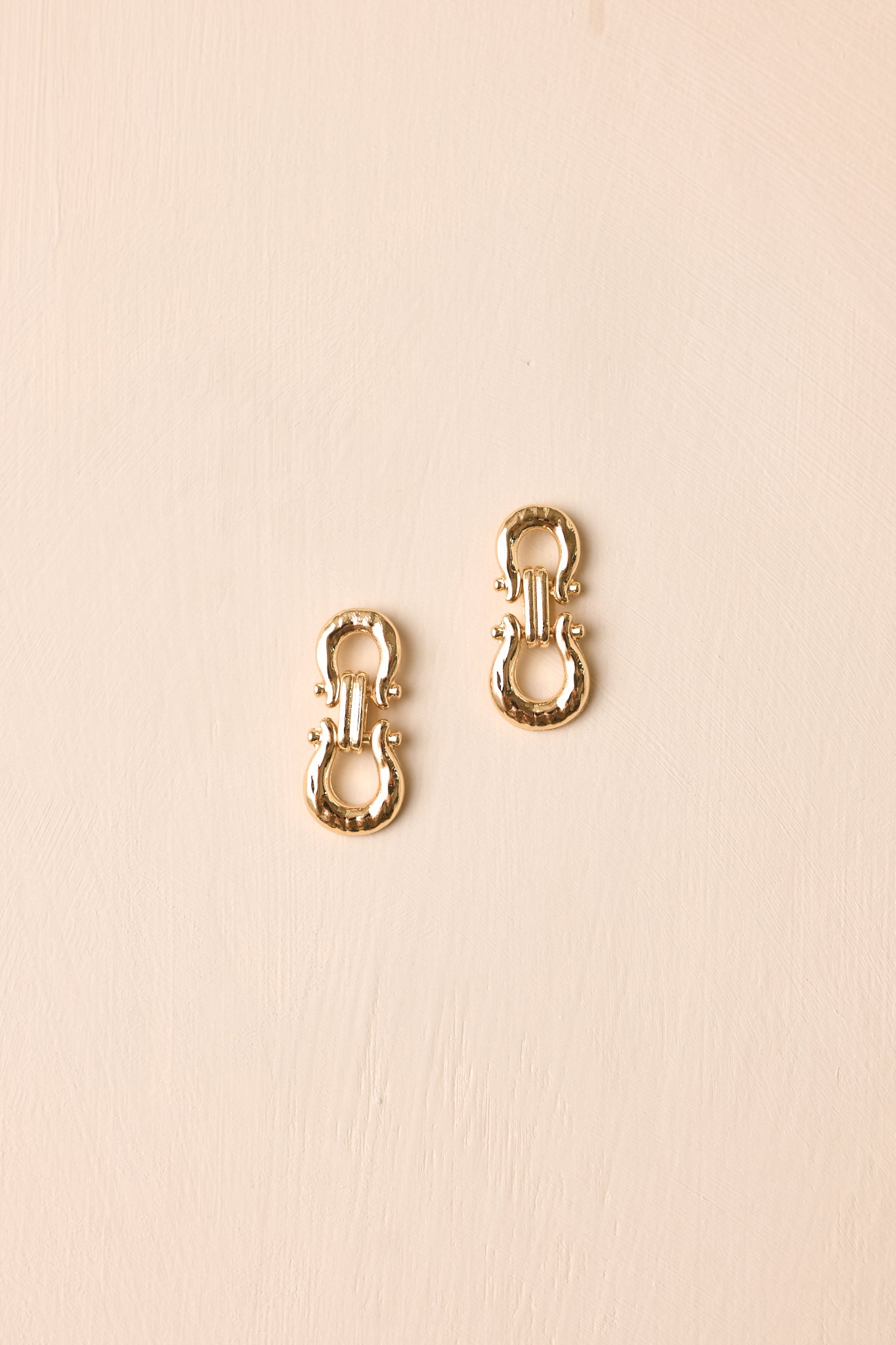 A pair of small gold-toned metal lobster clasp connectors with a textured finish, displayed on a light beige background.