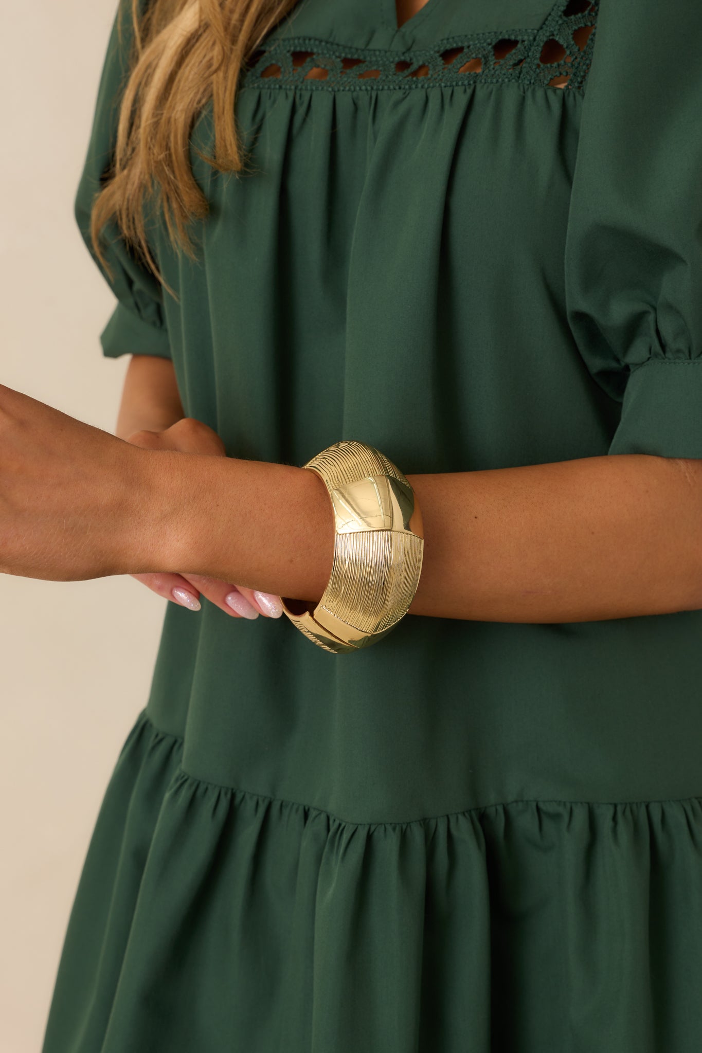 Cropped view of the gold cuff bracelet on wrist, highlighting the alternating smooth and engraved linear texture panels.
