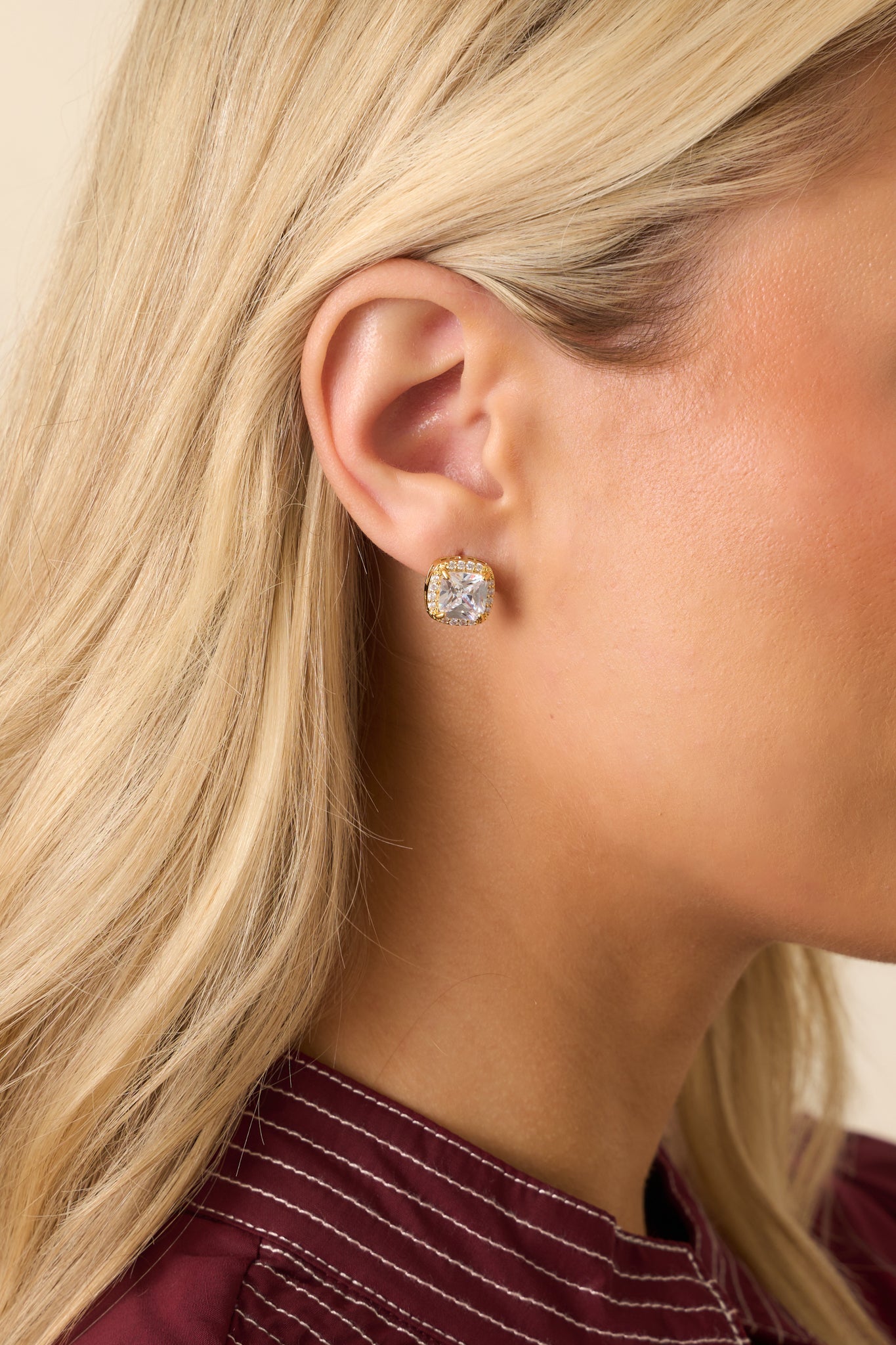 Cropped view of gold-dipped stud earrings featuring faceted cushion-cut cubic zirconia centers and pavé halo.