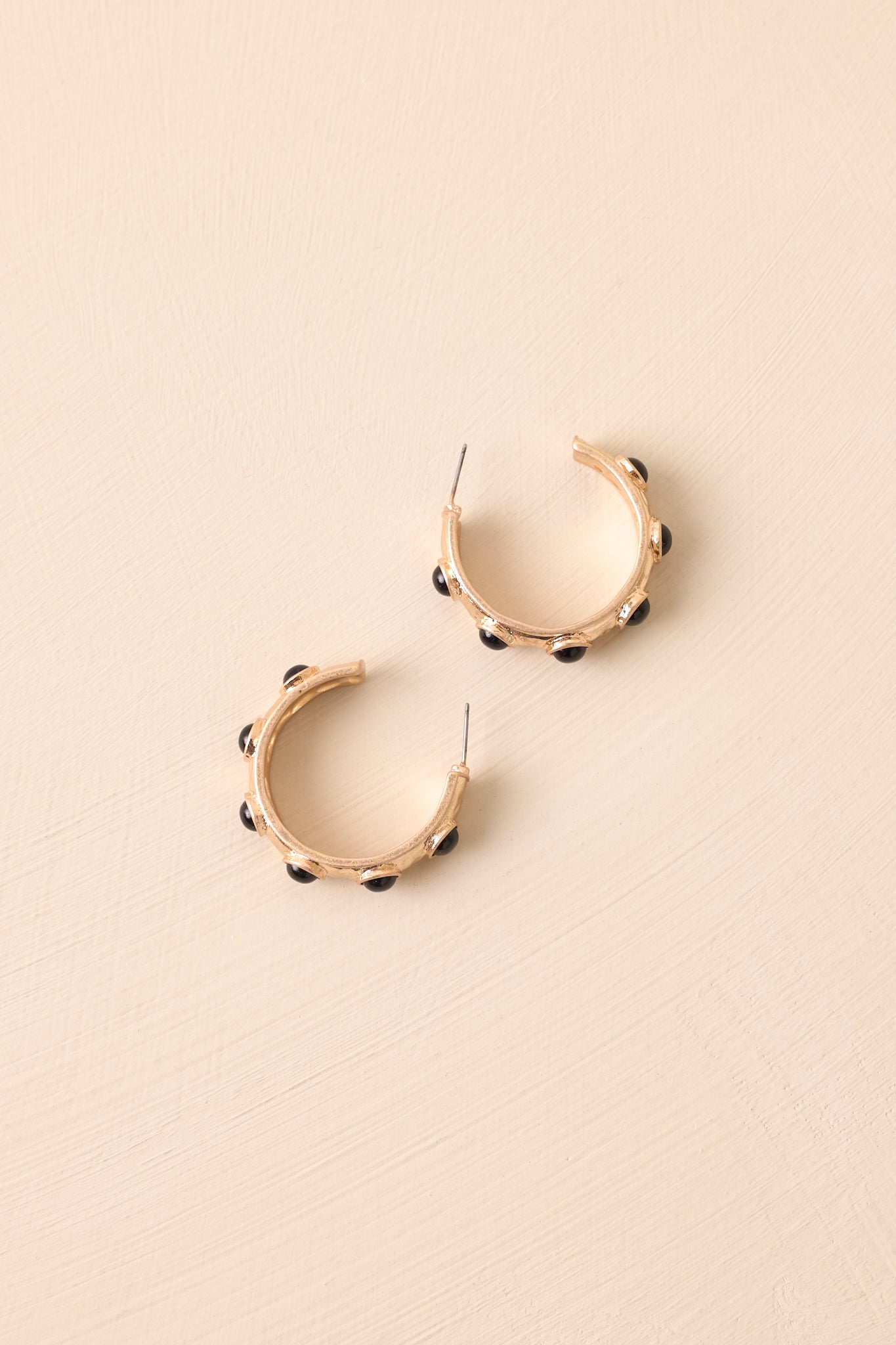 Angled flat lay of gold hoop earrings featuring circular black stone inlay and open c-shaped design.