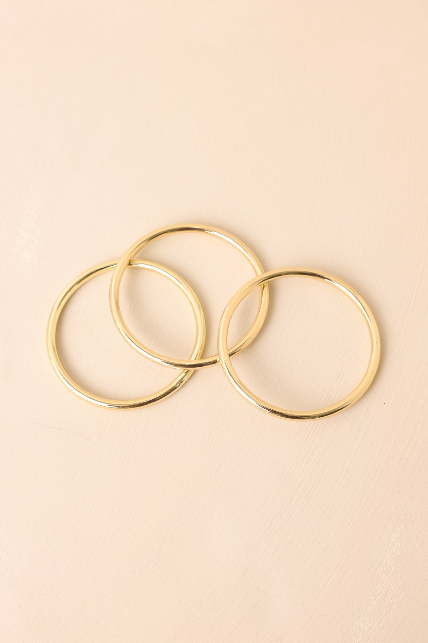 The set of three gold slip-on bangles with a polished finish shown against a beige background.