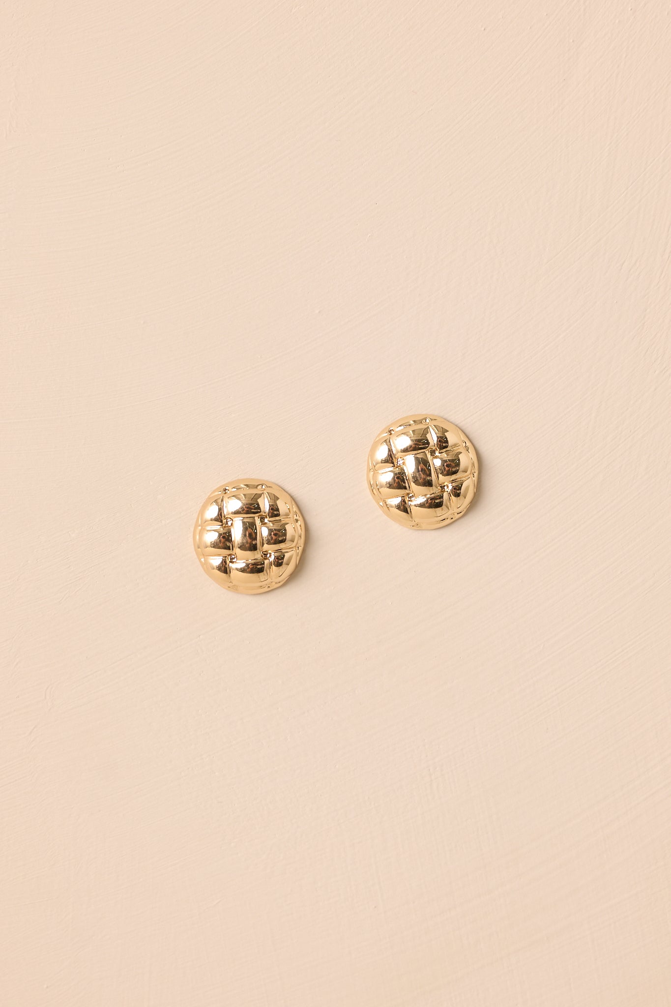Front View of gold earrings showcasing the circular dome shape and reflective shiny finish on beige background.