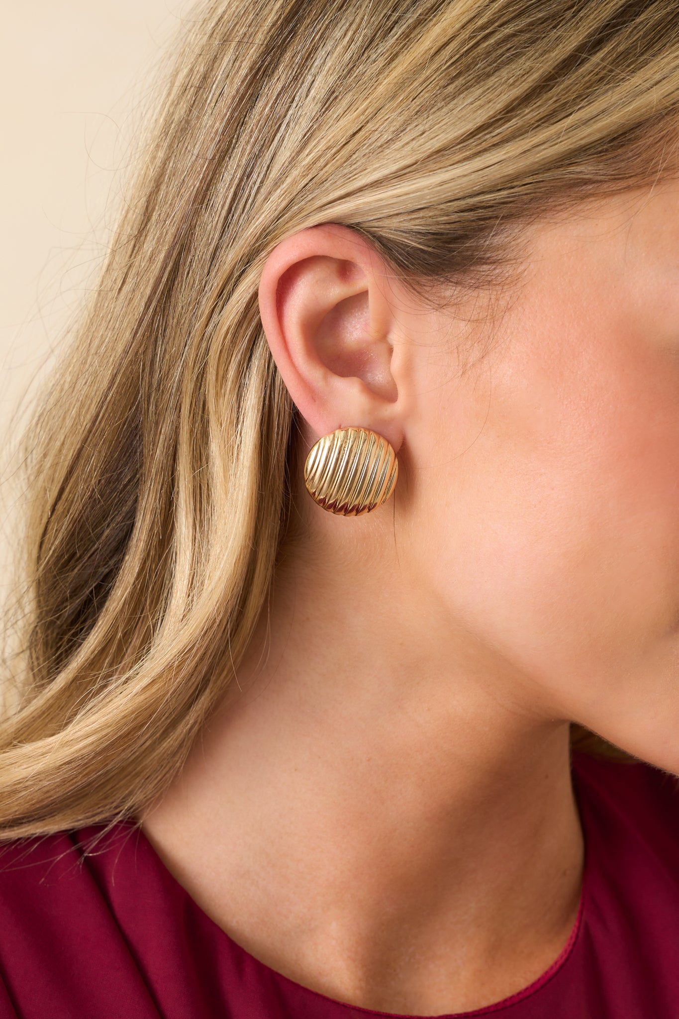 A side view of one gold earring, emphasizing the rounded shape and ribbed texture.