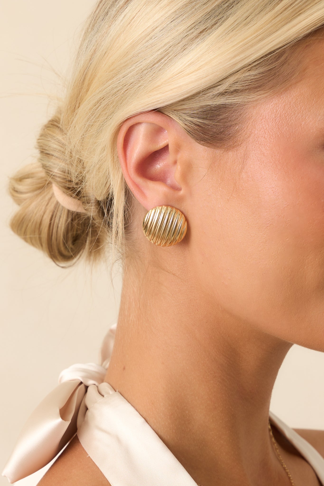 A close-up of a single gold earring revealing the fine ribbed texture and secure post backing.
