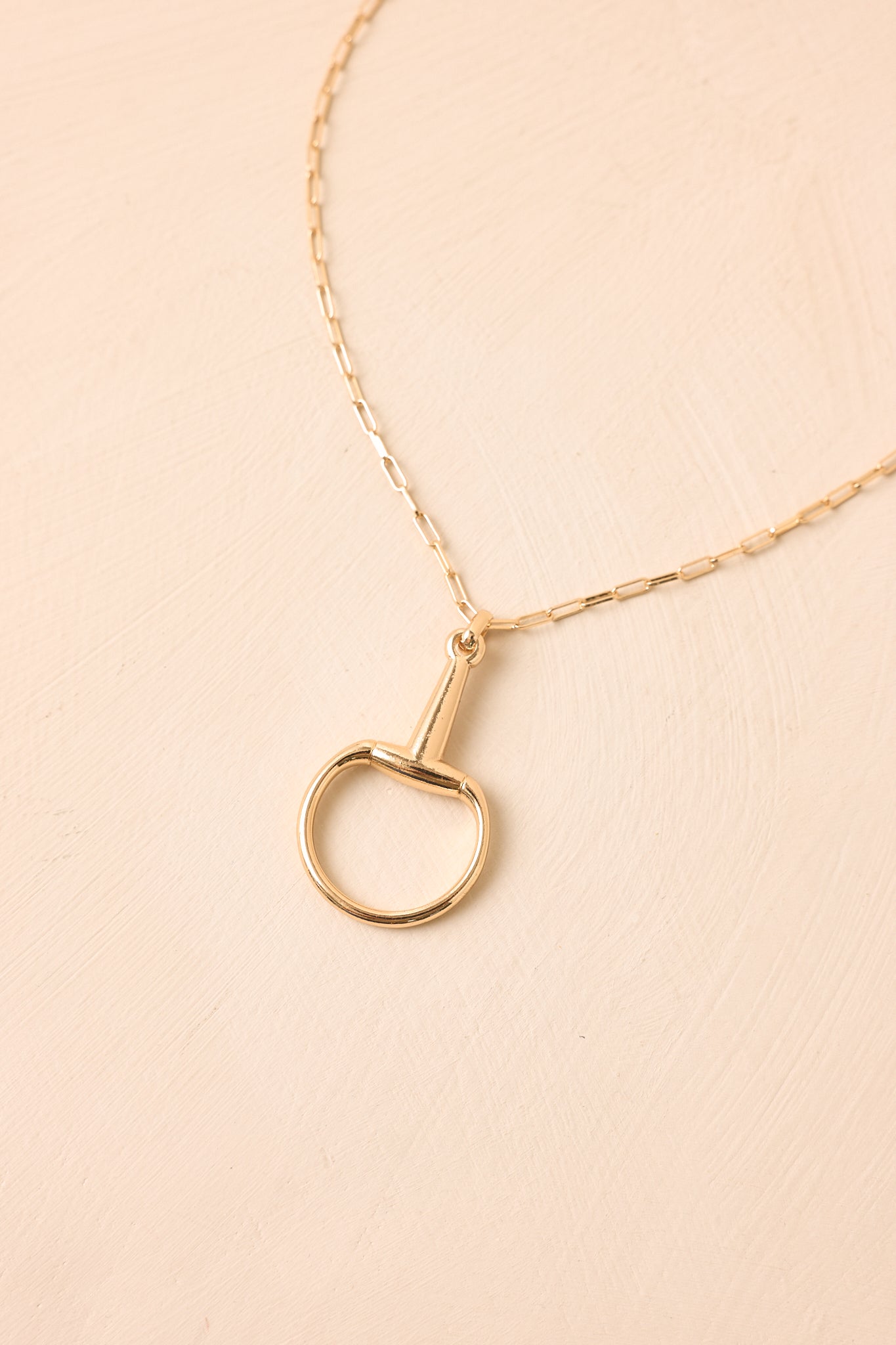 Close-up of a polished gold stirrup pendant necklace on a fine paperclip chain.