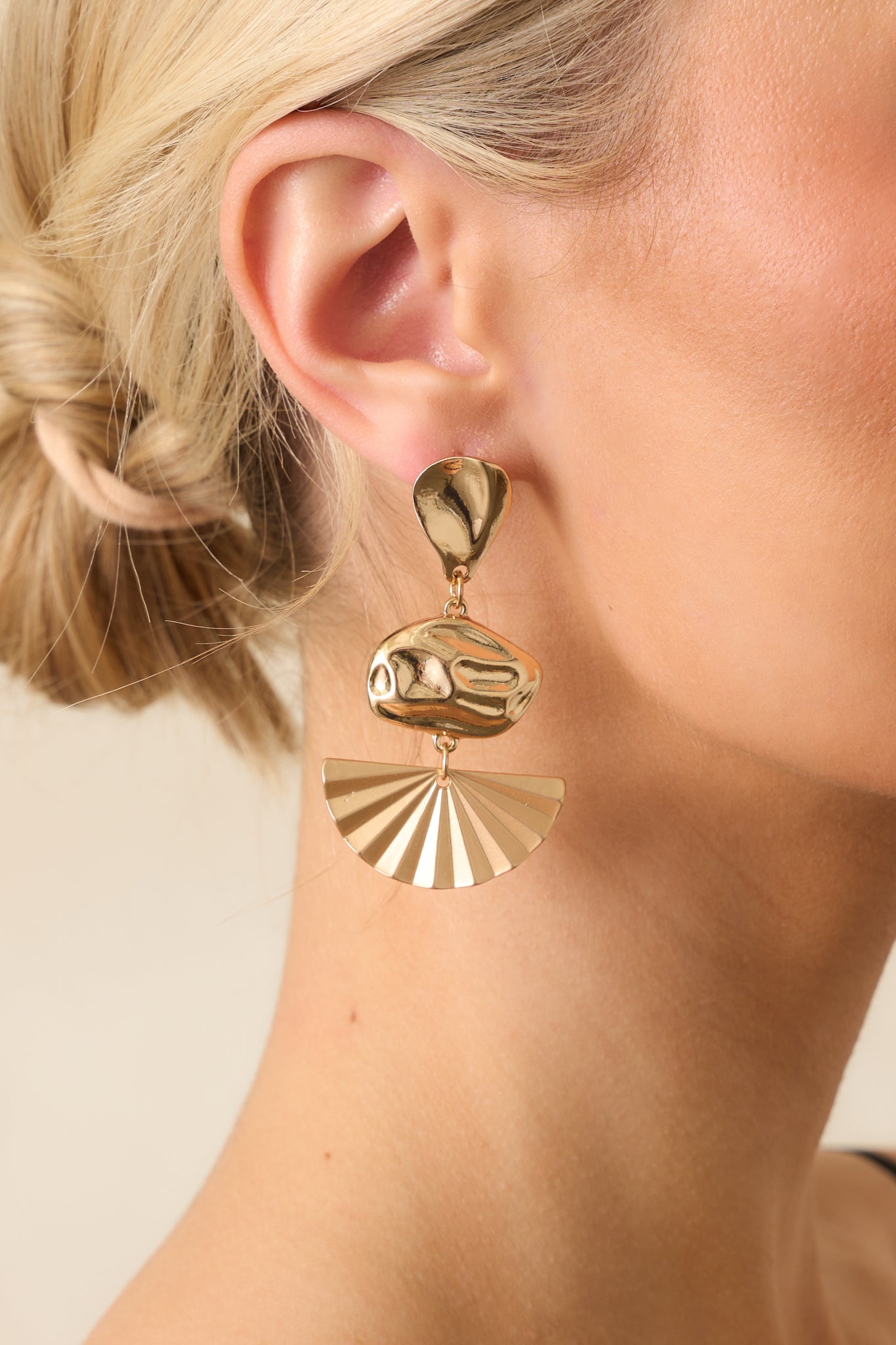 Extreme close-up of one earring showing the teardrop stud, oval middle charm, and fan-shaped charm joined by gold jump rings with a matte textured finish.