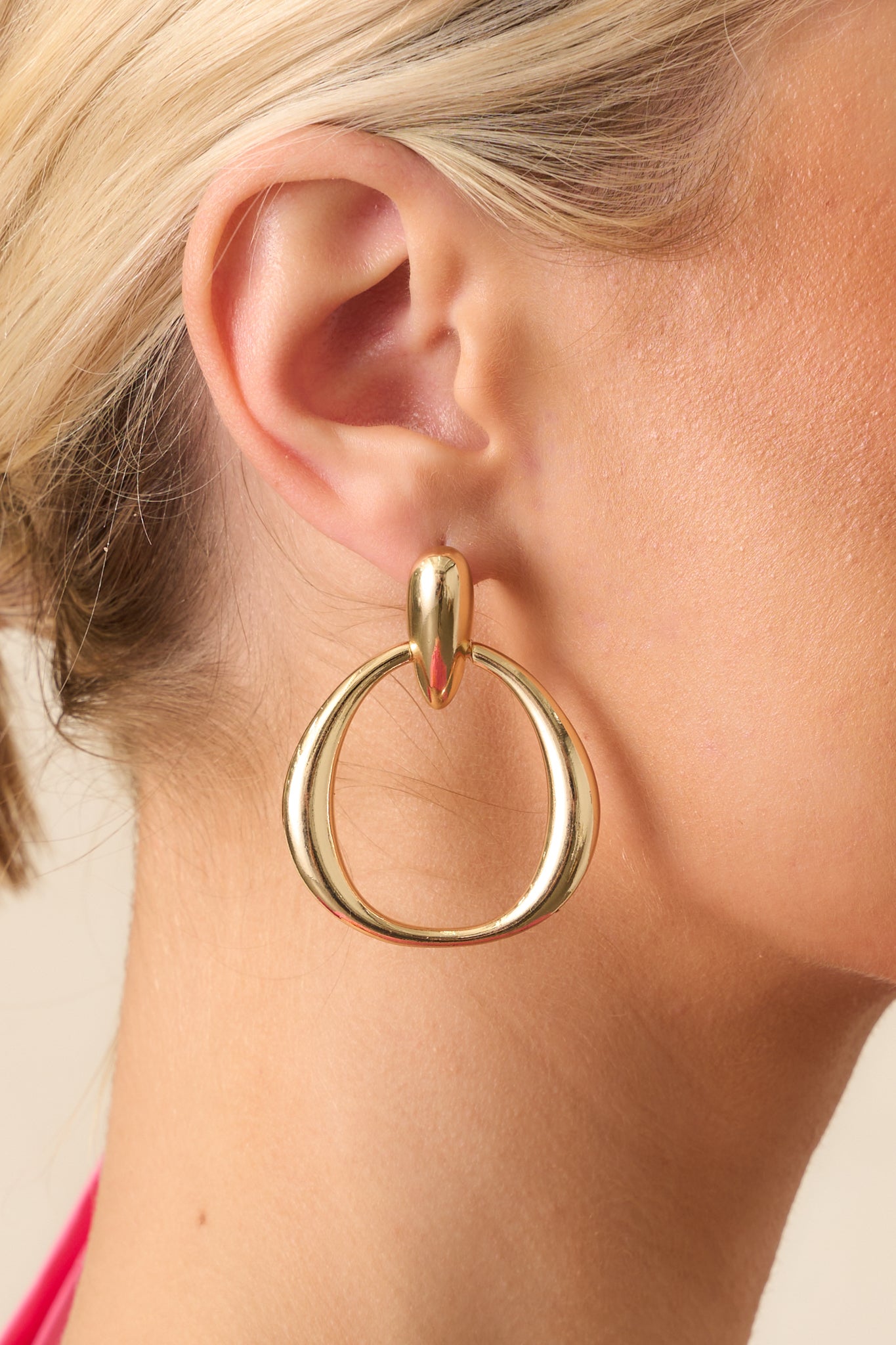 Closeup of gold teardrop stud earrings with circular drop link on model.