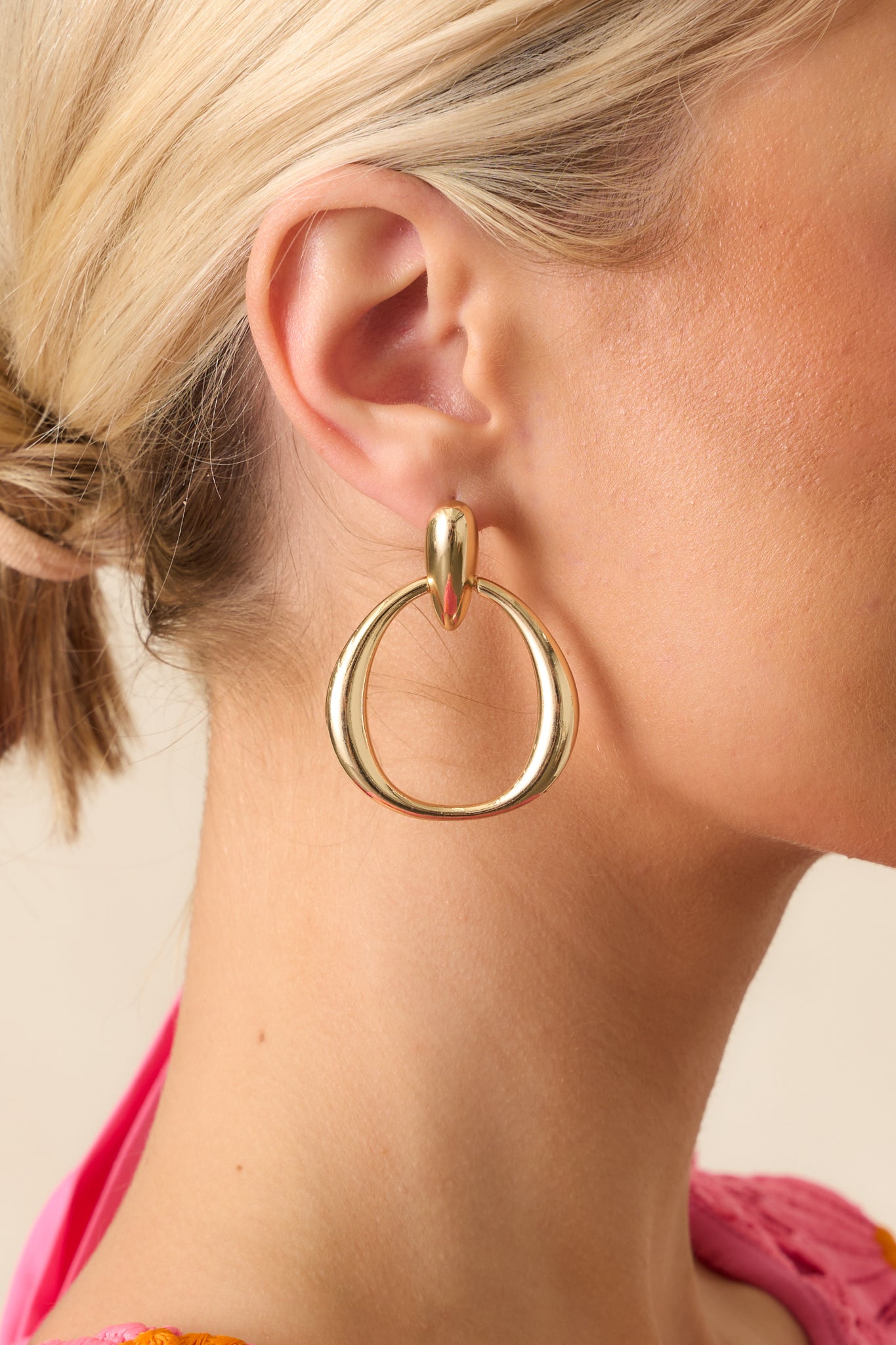 Gold teardrop stud earrings with circular drop link shown on model.