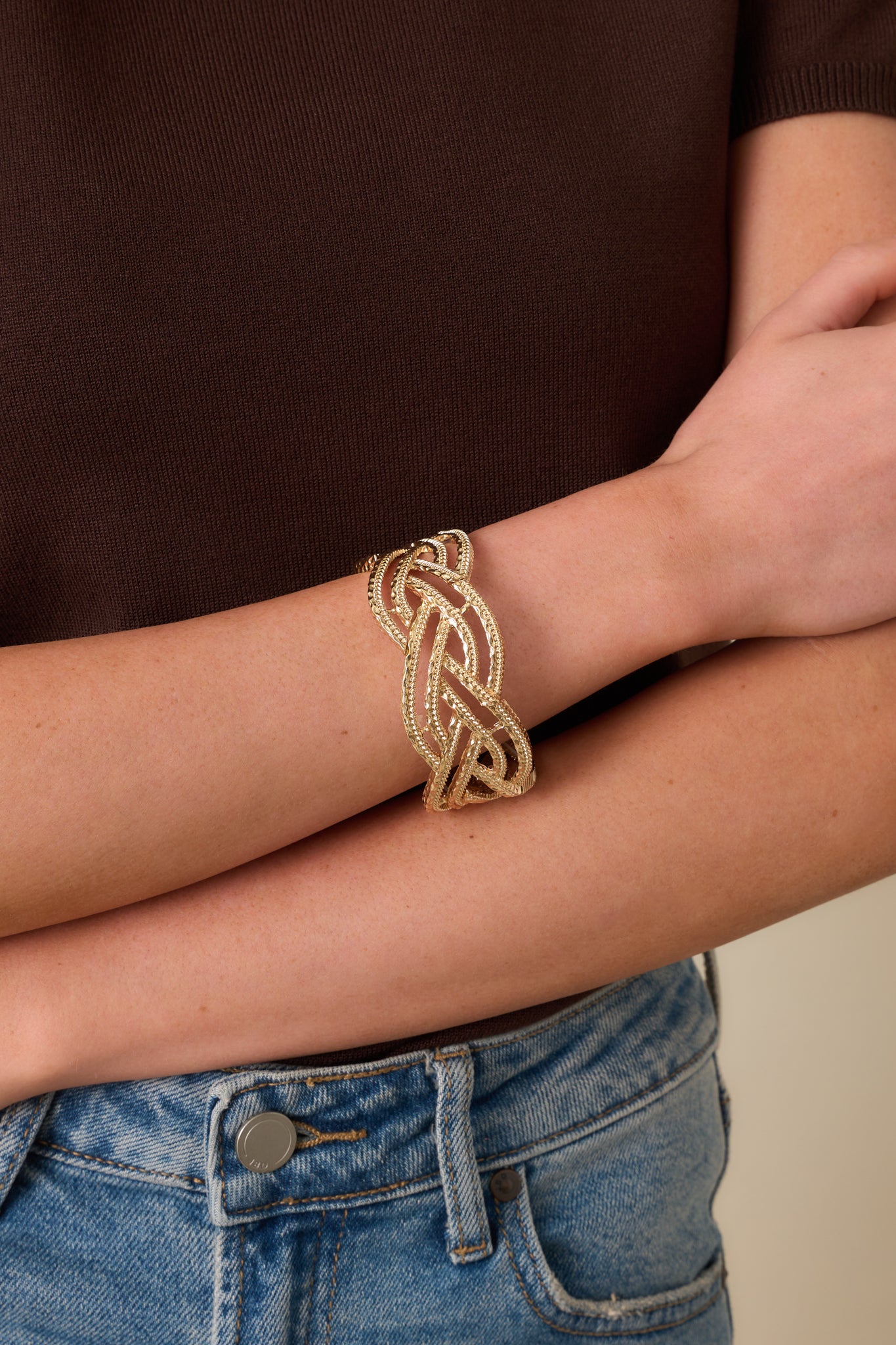 Cropped view of the gold bracelet highlighting the open braided design and curved structure.