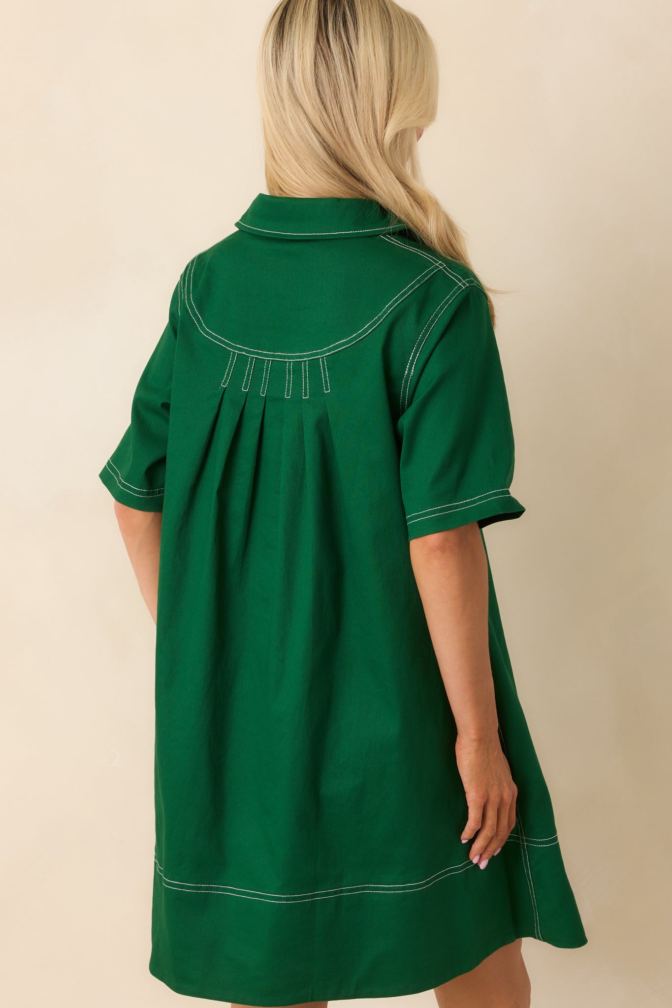 A back view of the kelly green mini dress featuring continuous white topstitching and a clean, structured finish.