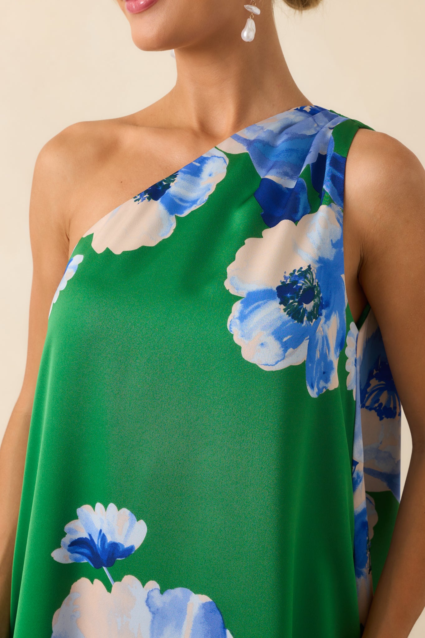 A close-up image showing the blue floral print and texture of the green satin fabric near the neckline and shoulder area.