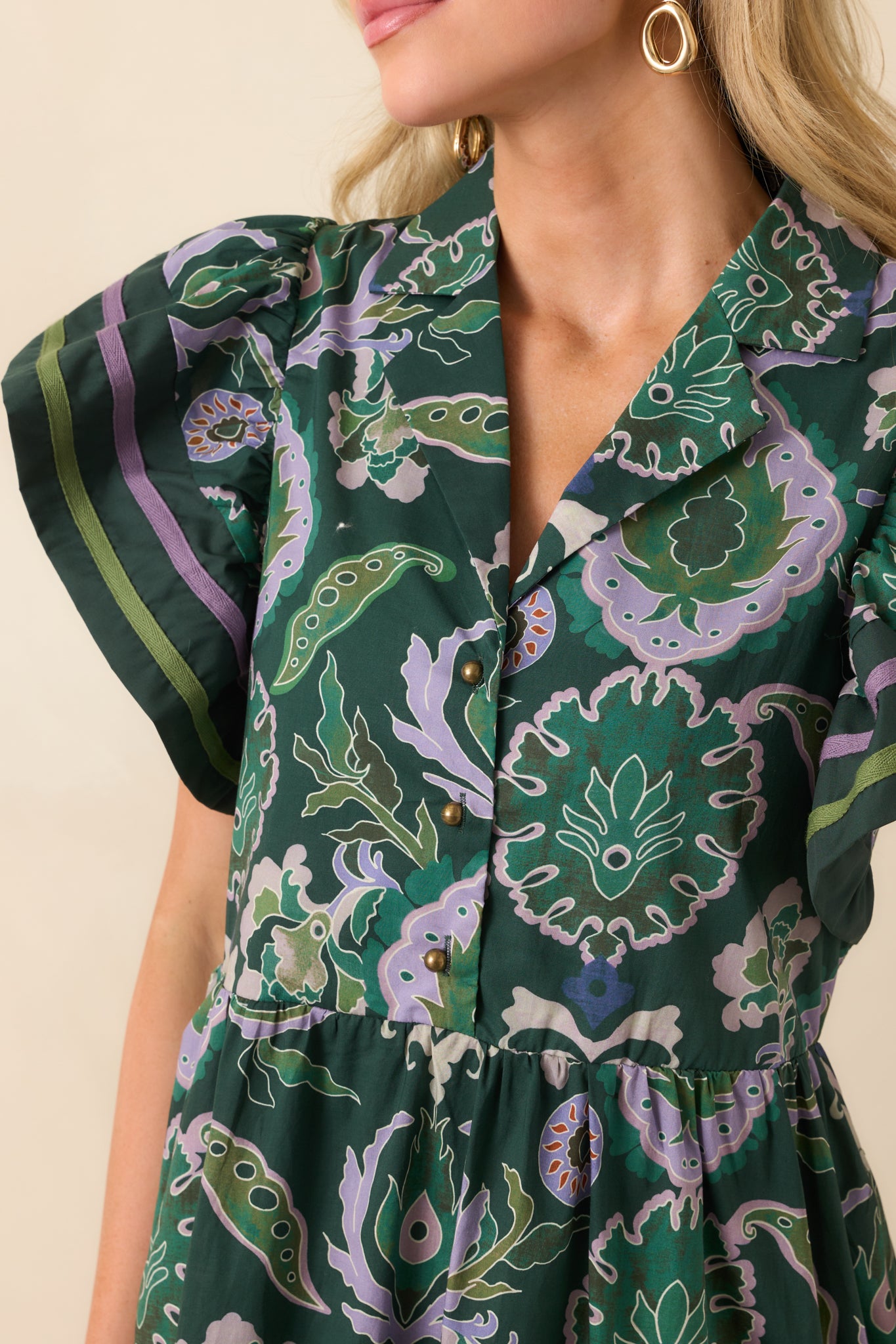 Zoomed-in image showing the notched collar, v-neckline, button front, and green and purple trim details.