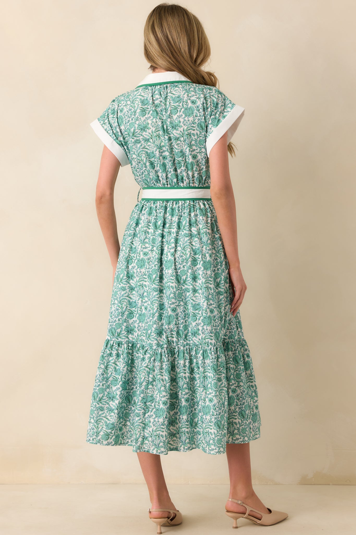 A view from behind showing the green floral midi dress with short sleeves, white cuffs, and a relaxed fit.