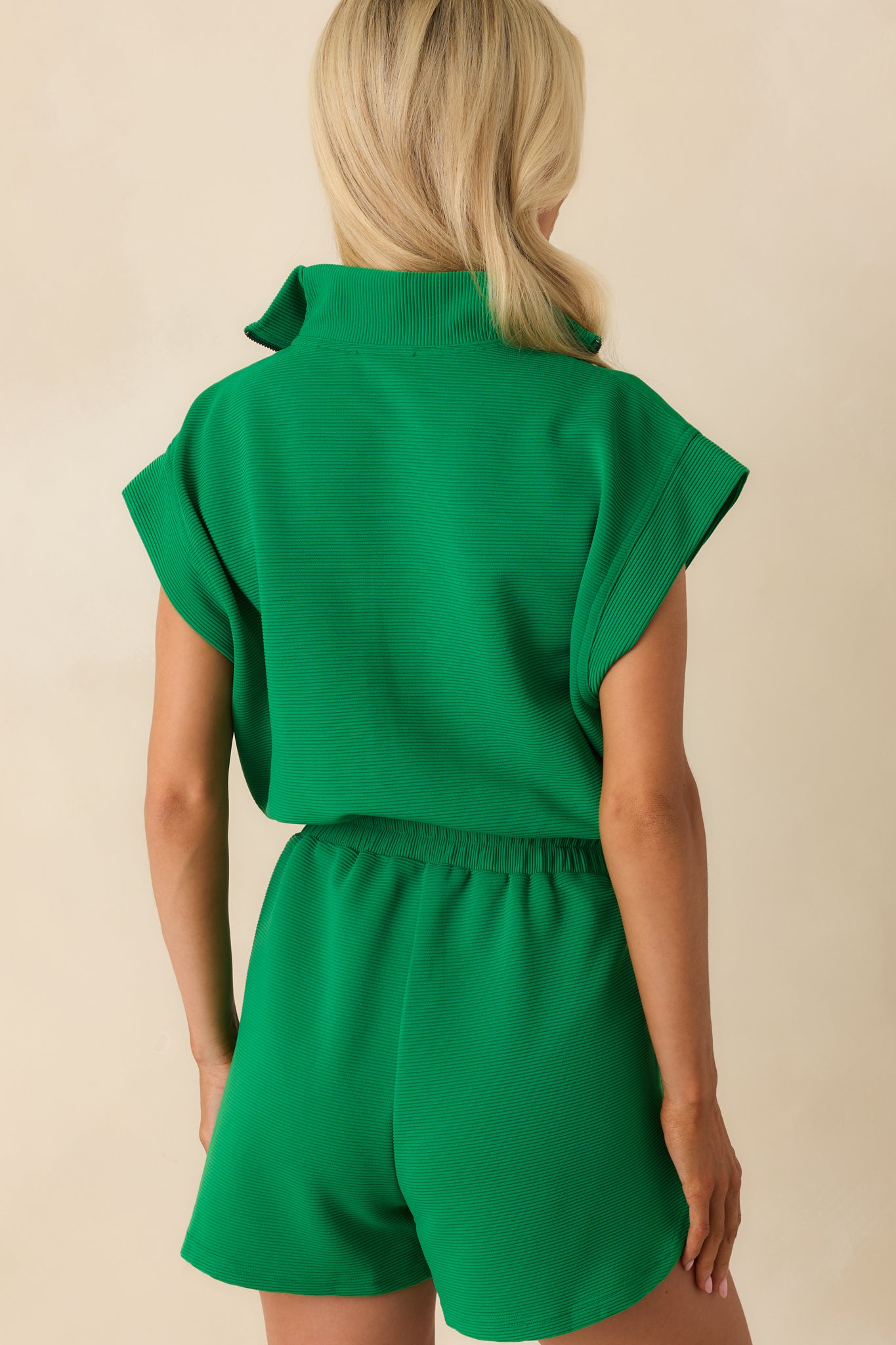 A view from behind of the green romper, showing the continuation of the ribbed texture and the relaxed fit through the shoulders and waist.