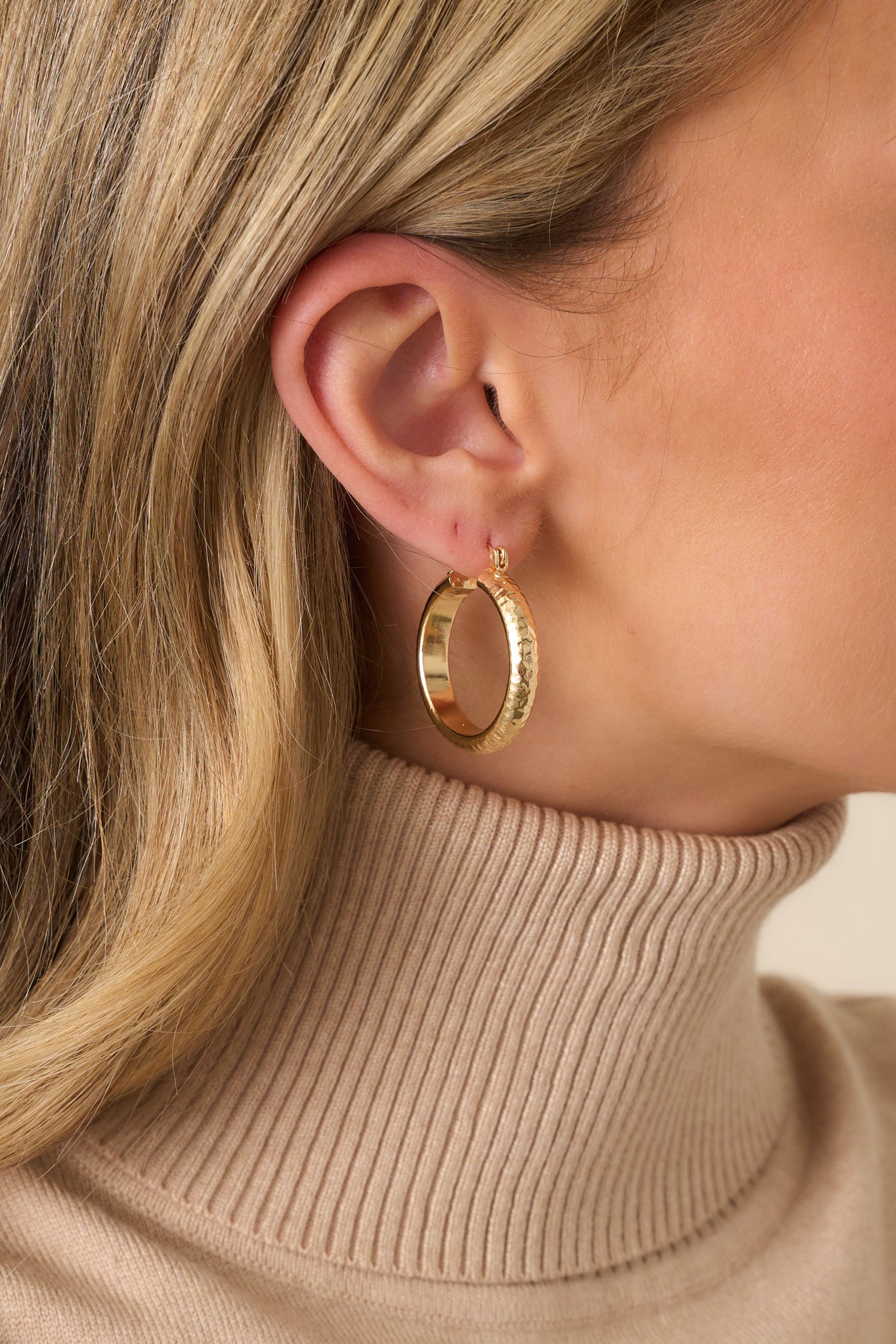 A cropped view of the gold earrings showing the curved shape and hammered texture across the surface.