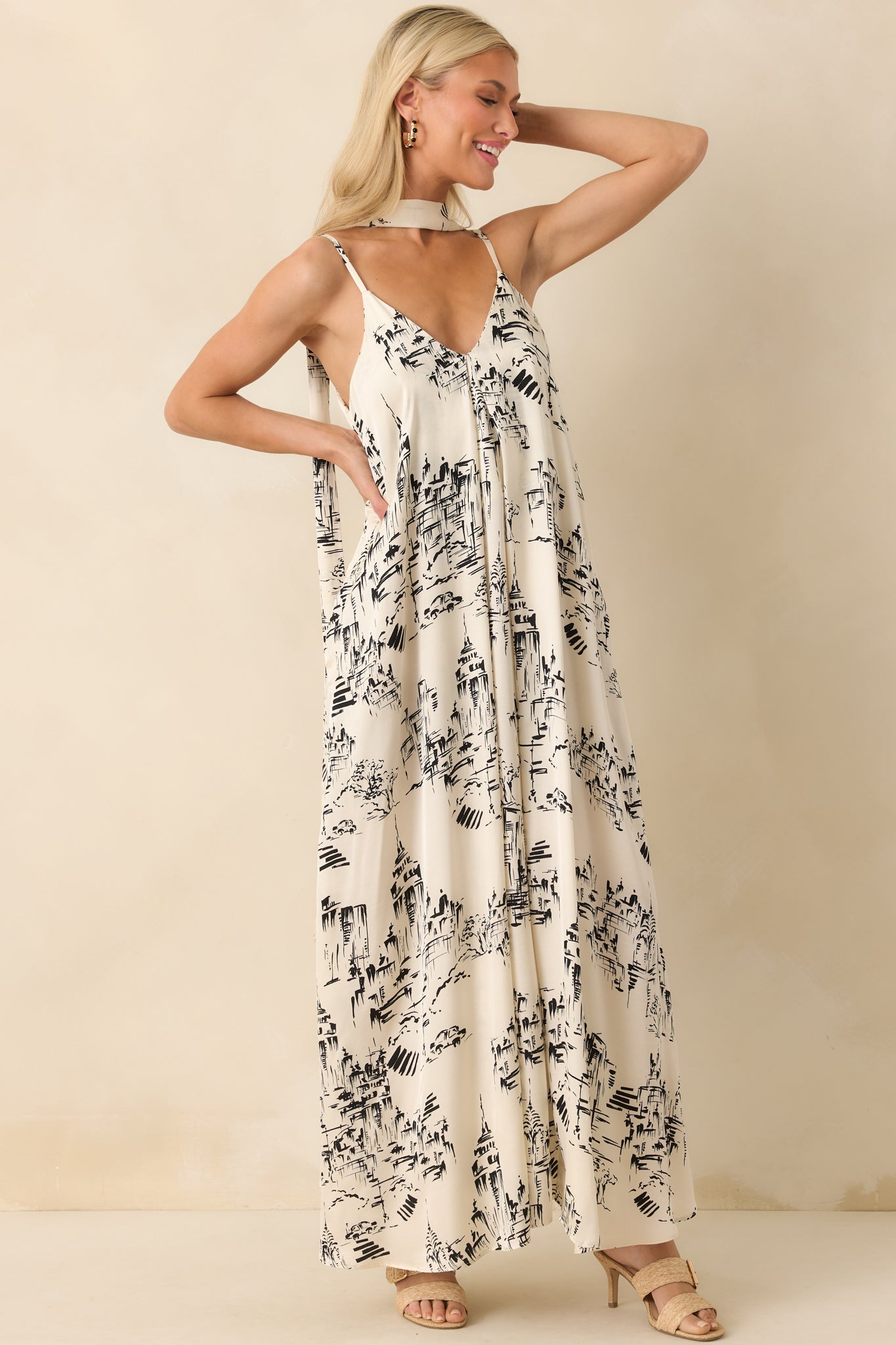 Front-facing full view of the ivory maxi dress featuring a black scenic sketch-style print, deep V-neckline, and adjustable spaghetti straps.