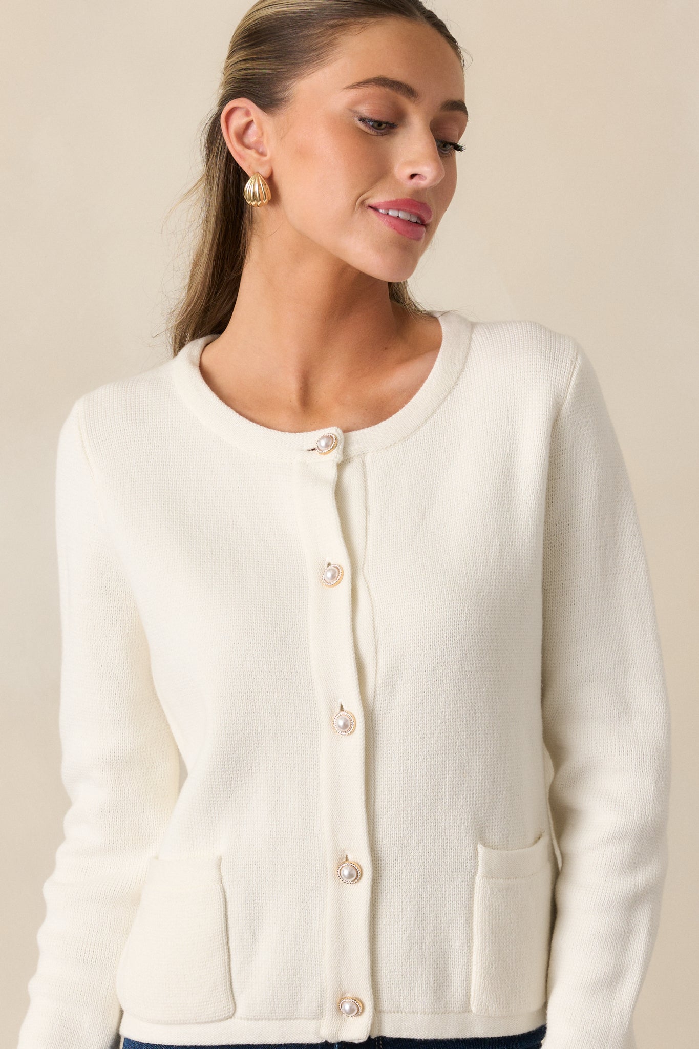 Cropped view of ivory cardigan showing faux pearl buttons and crew neckline.