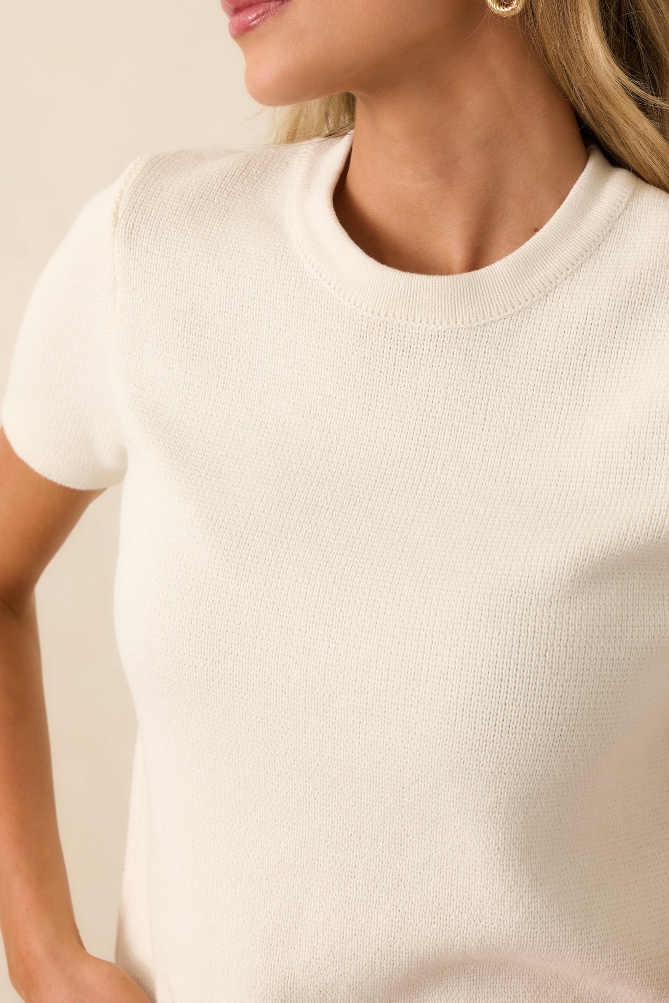 Close-up of ivory sweater displaying knit texture and crew neckline stitching.