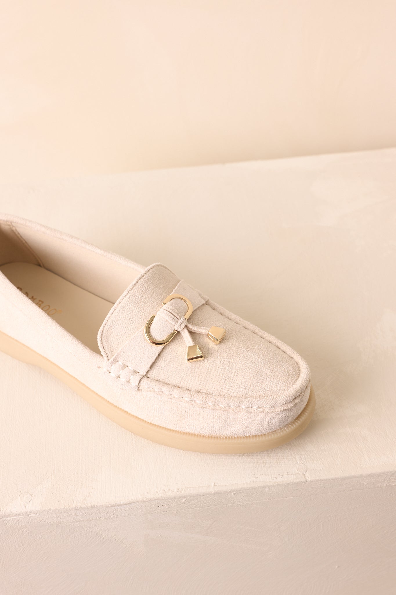 A detailed shot of the ivory loafers emphasizing faux suede fabric, a gold charm, and saddle strap design.