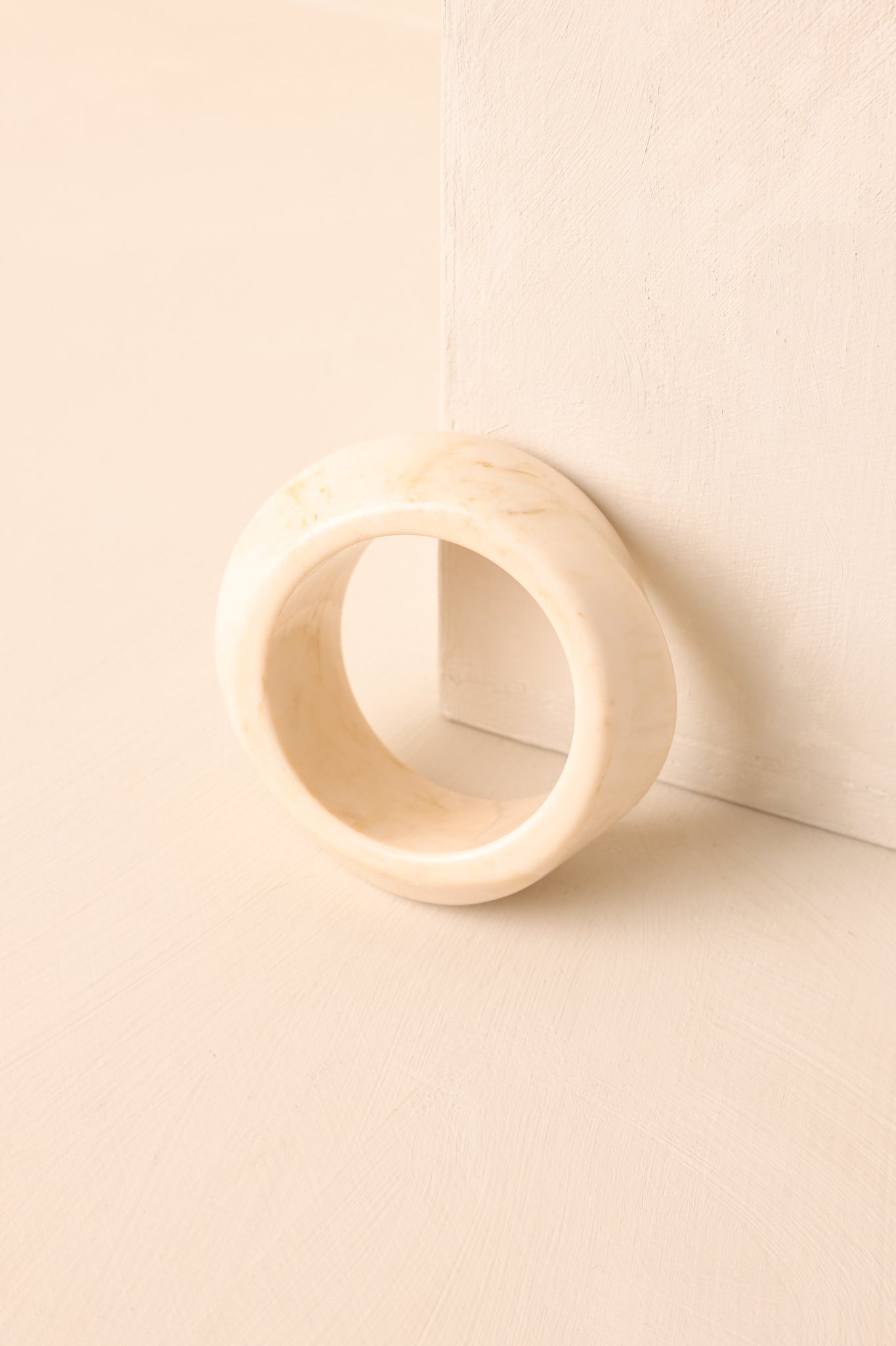 The ivory marbled acrylic bangle displayed upright on a beige background highlighting its retro-inspired design.