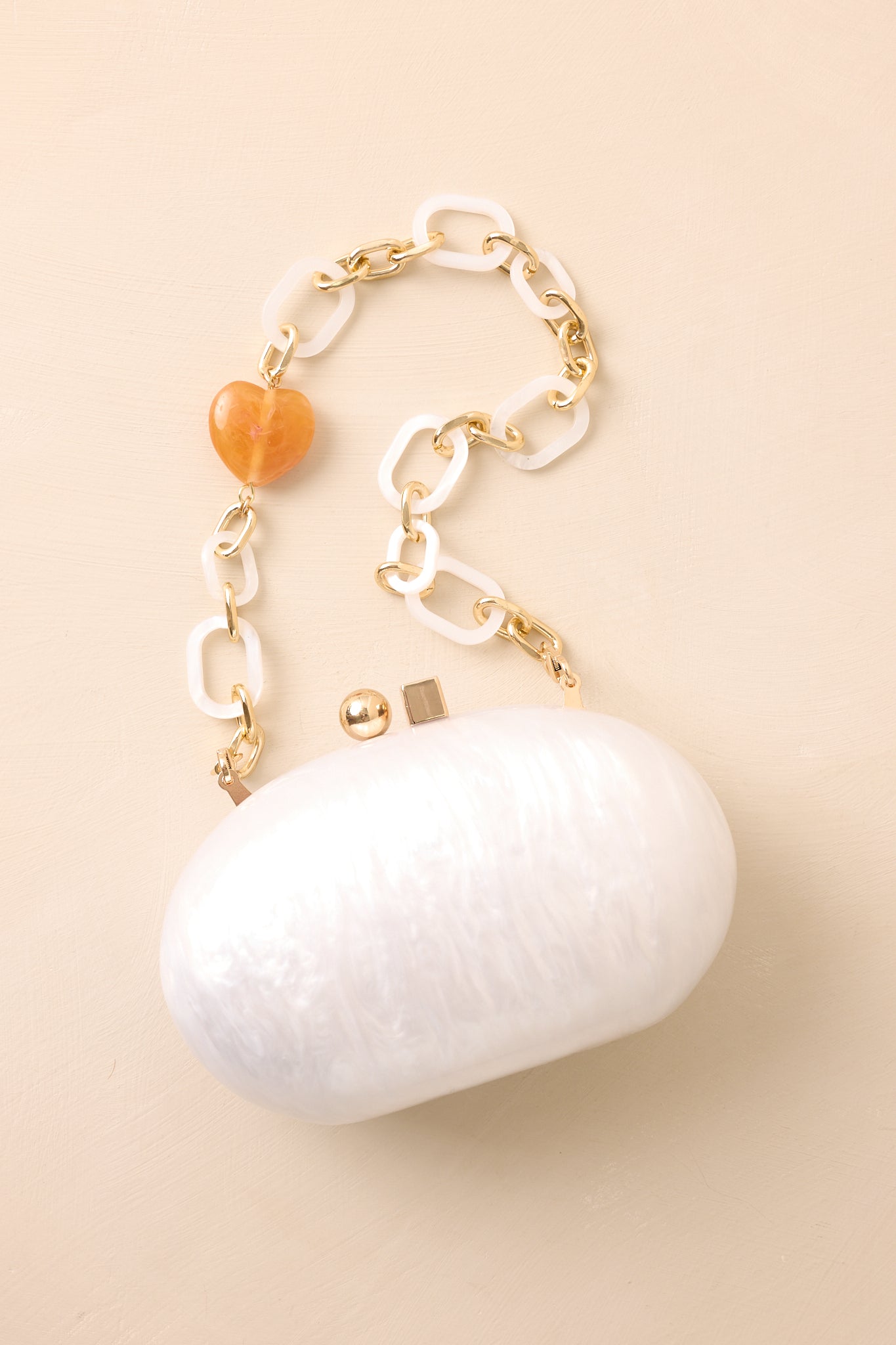 Ivory clutch bag with a pearlescent glossy finish and gold box clasp laid flat against beige background.