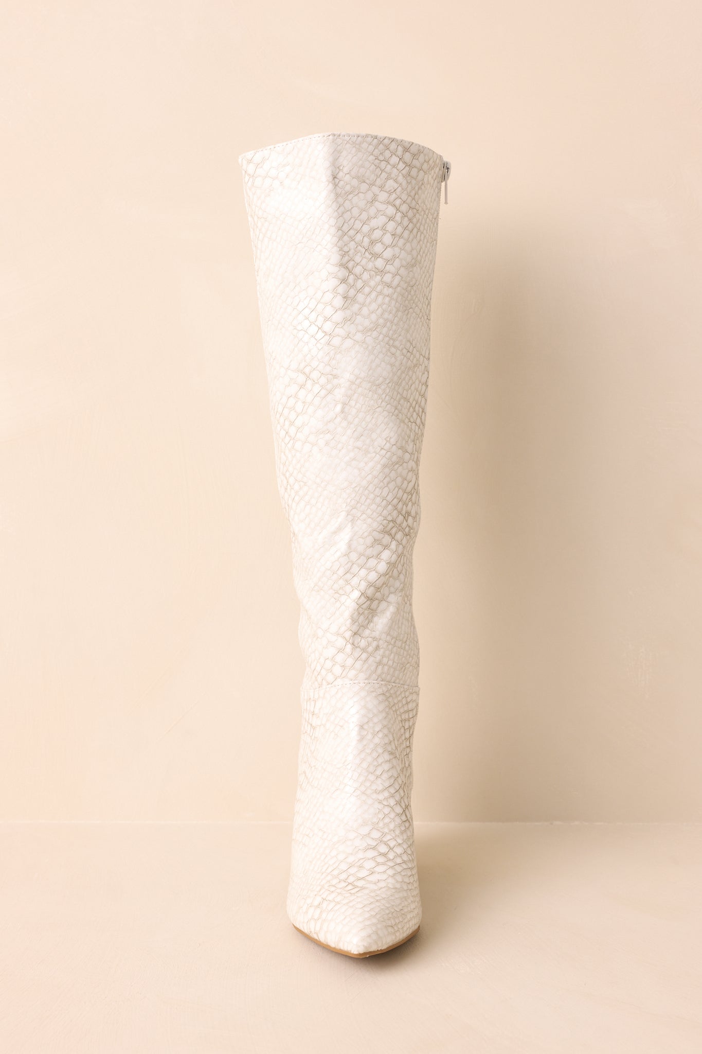A front-facing view of the ivory snakeskin embossed boots with pointed toes and a paneled detail.
